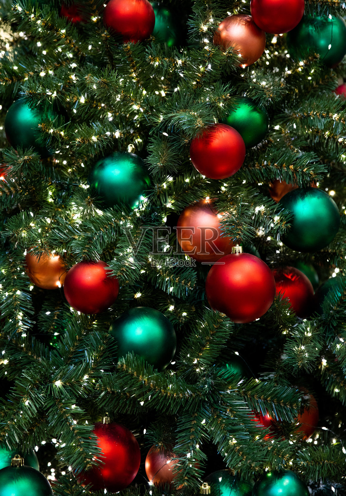 明亮闪亮的红色、绿色、橙色球形玩具和灯光装饰在绿色室内圣诞树上，迎接新年。照片摄影图片