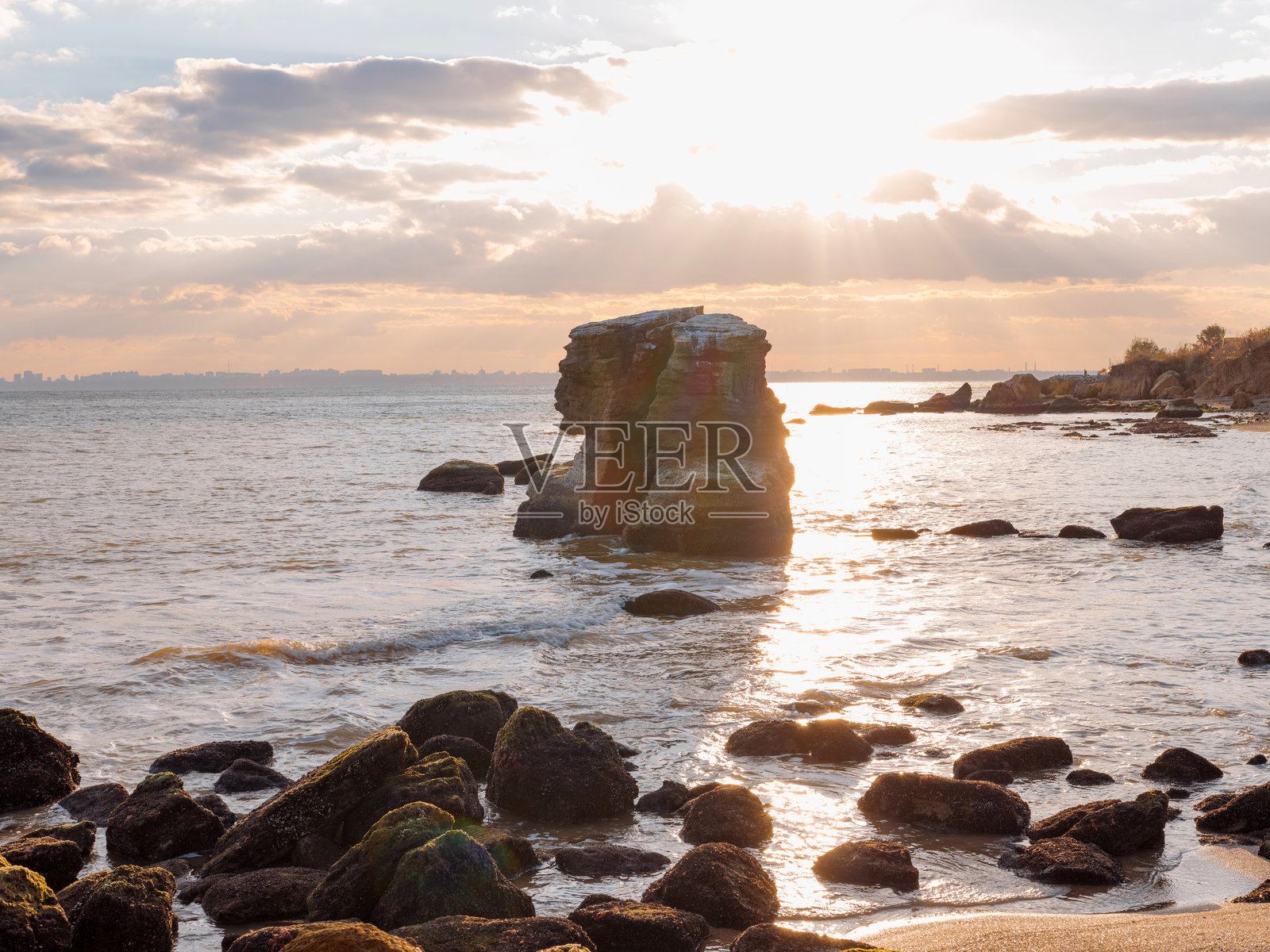 黑海海岸日落时美丽的海景，岩石和阳光透过云层洒下光芒。照片摄影图片