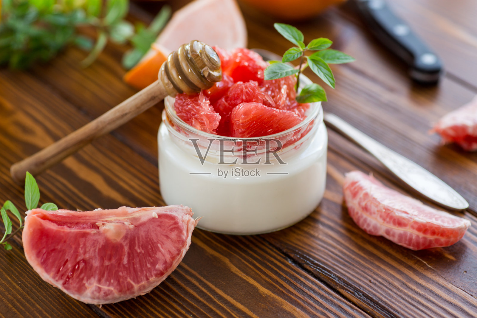 自制甜酸奶装在玻璃罐中，里面有红色成熟的葡萄柚块和蜂蜜，放在木桌上。照片摄影图片