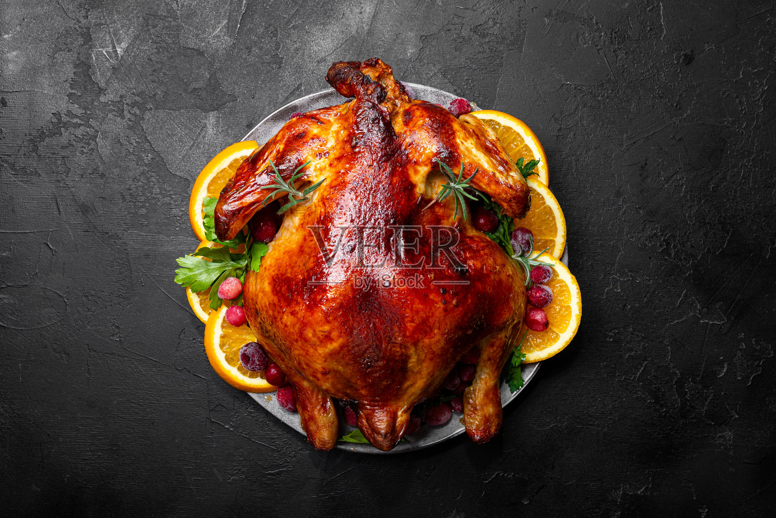 黑色背景上的整只圣诞烤鸡，配有蔓越莓和橙子，俯视图照片摄影图片