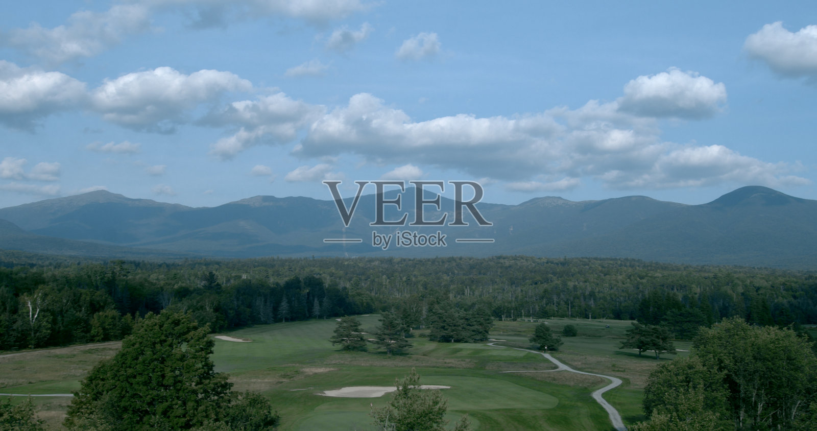 森林和高尔夫球场后方的山脉在多云的蓝天下照片摄影图片