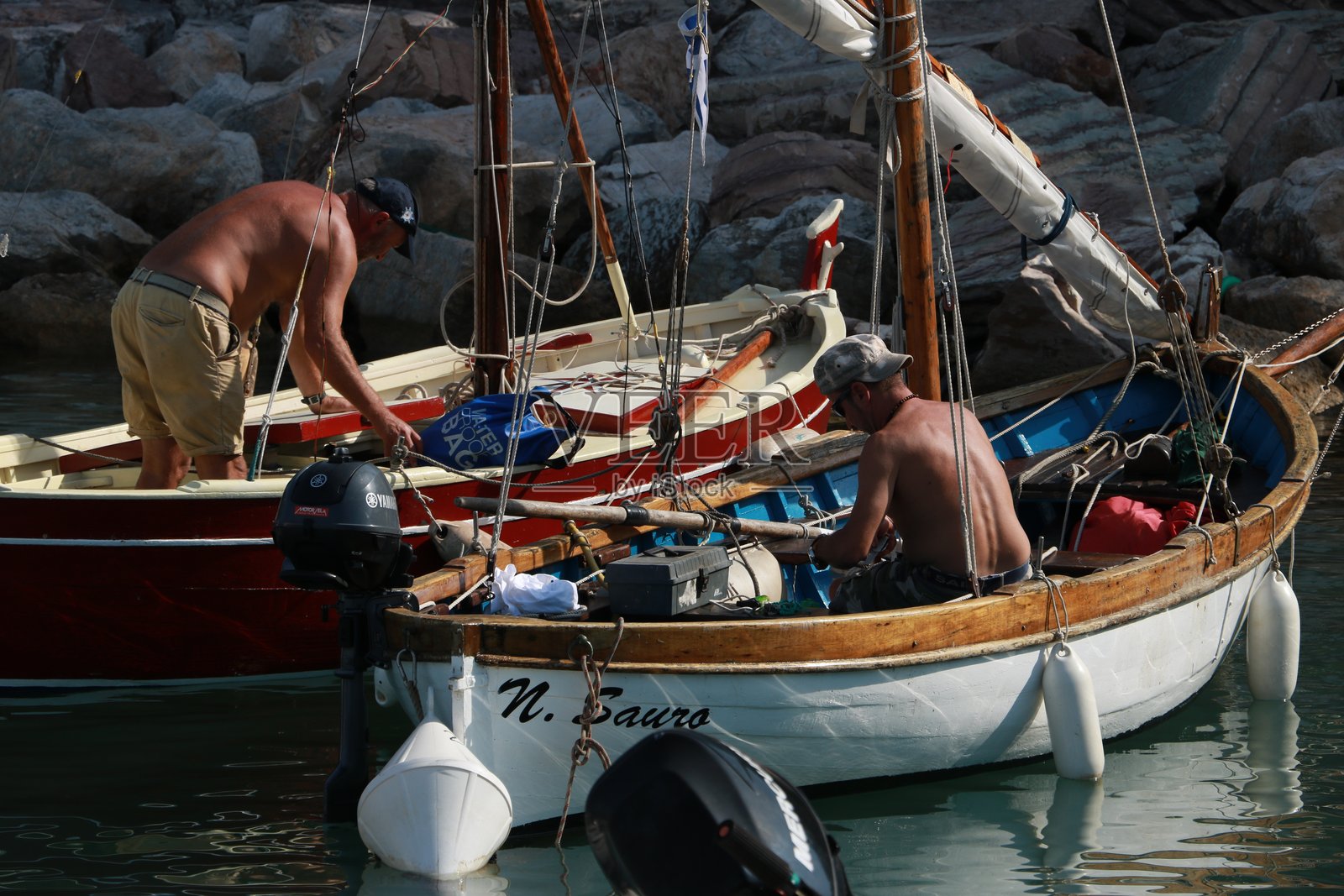 色彩斑斓的渔船停靠在港口。两位渔民正在准备出航。照片摄影图片