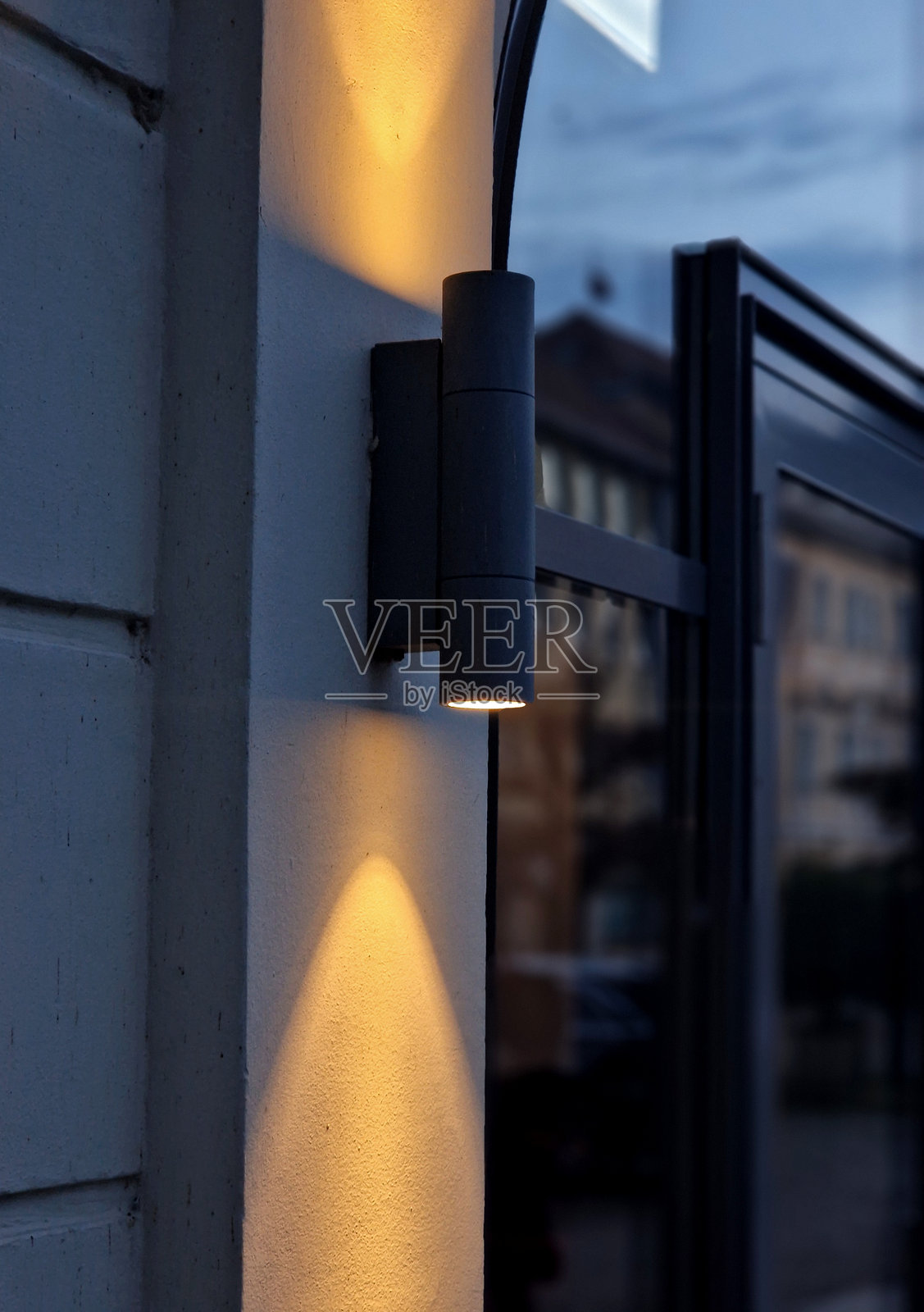 壁灯在夜晚以锥形光束照亮房屋外立面的墙壁。黑色的晚间定位和导航灯在石笼墙上向两个方向发光，表面涂有粉末涂料。照片摄影图片