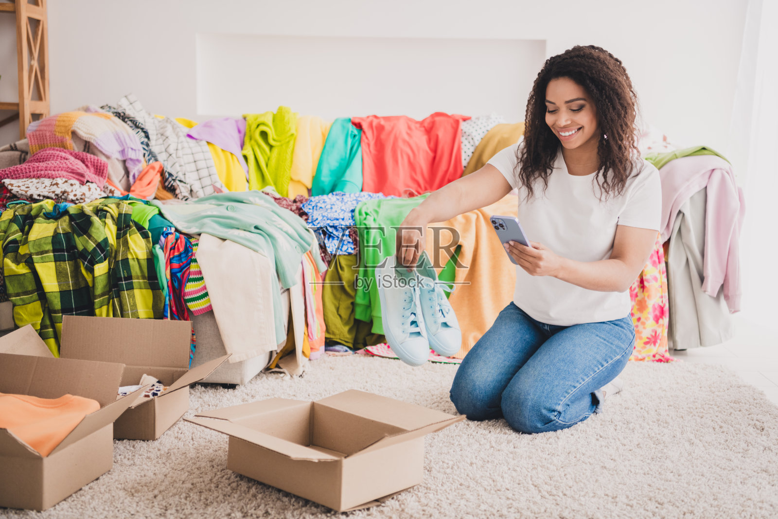 年轻女性在客厅里展示待售衣物，使用手机列出捐赠或慈善活动的物品照片摄影图片