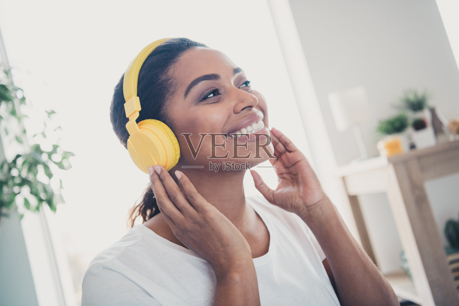 年轻女性的肖像，手触耳机，穿着衬衫，现代室内公寓环境。照片摄影图片