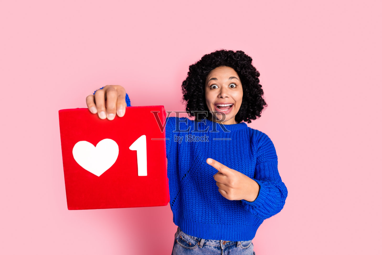 年轻女士手举社交媒体点赞图标，庆祝频道首次达到一百万，背景为粉色。照片摄影图片