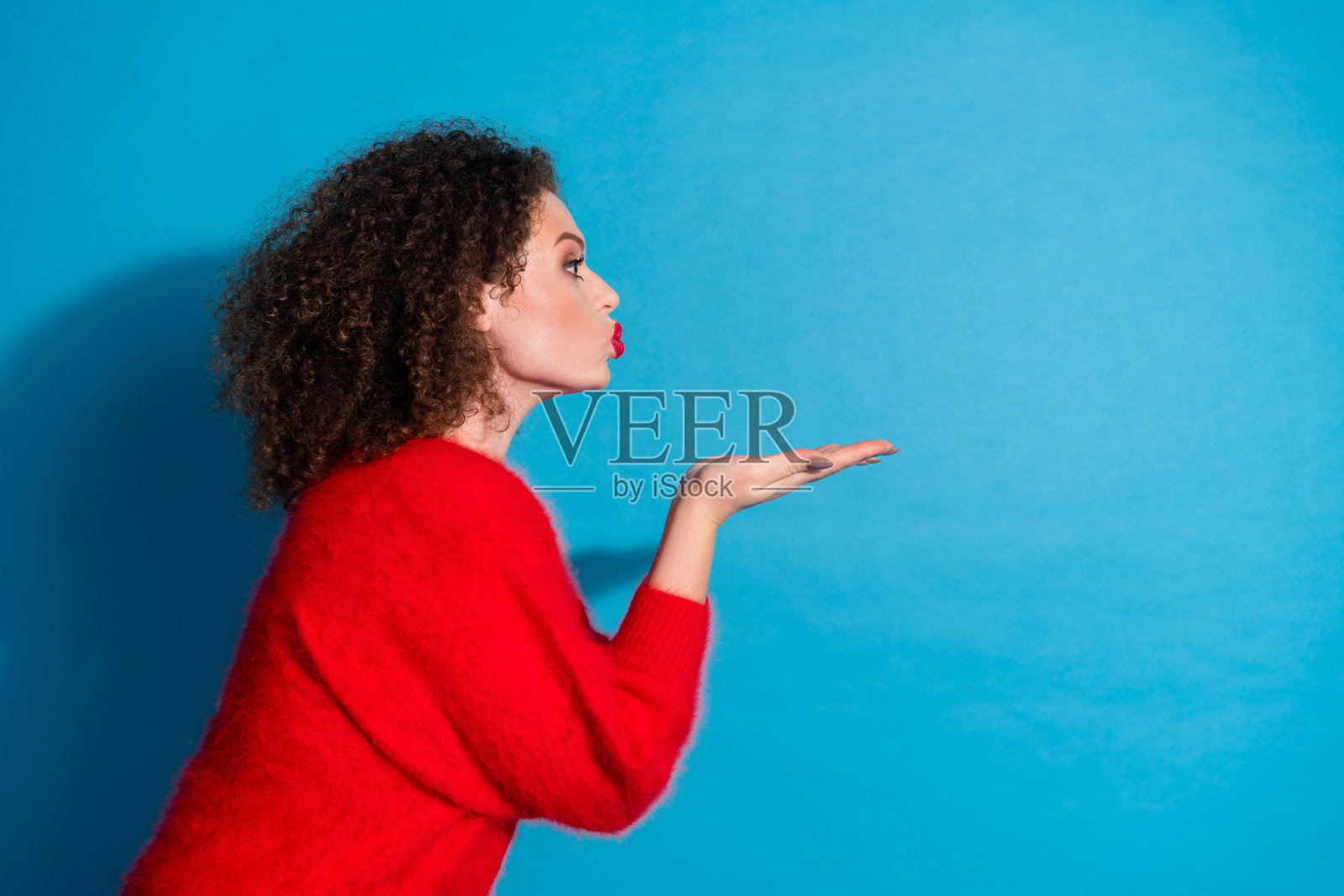 漂亮年轻女孩的照片肖像，向空旷的空间送出空气吻，穿着时尚的红色服装，背景为蓝色。照片摄影图片