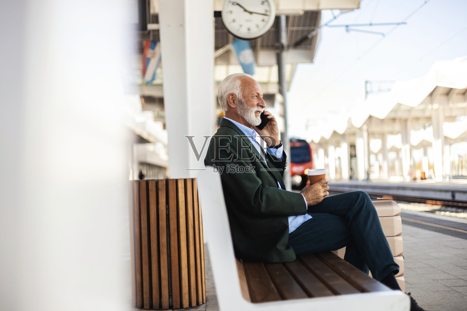 帅气的男士在出差，坐在行李旁边，在火车站用手机通话。出差的商人正在打电话。火车站微笑的商人照片。照片摄影图片
