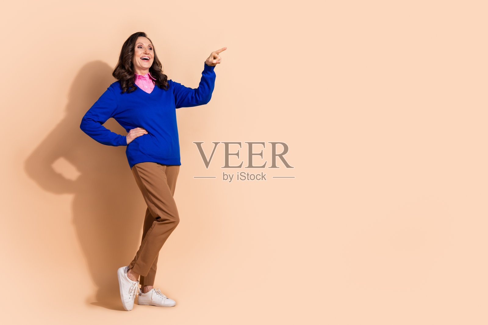 穿着蓝色时尚服装的迷人女性在米色背景前凝视空旷的空间。照片摄影图片