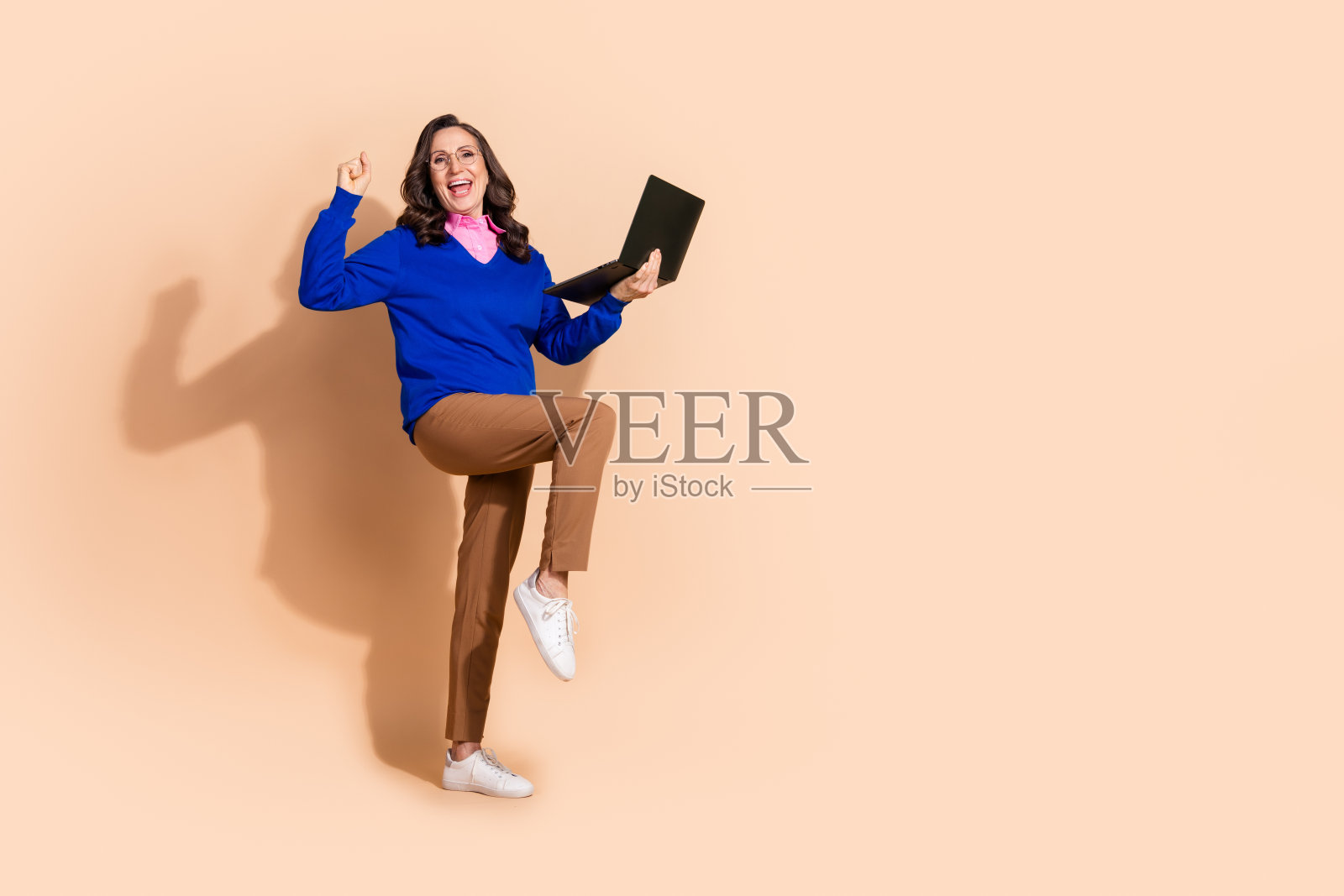 穿着蓝色时尚服装的快乐老年女性，手持设备，背景为空白的米色。照片摄影图片