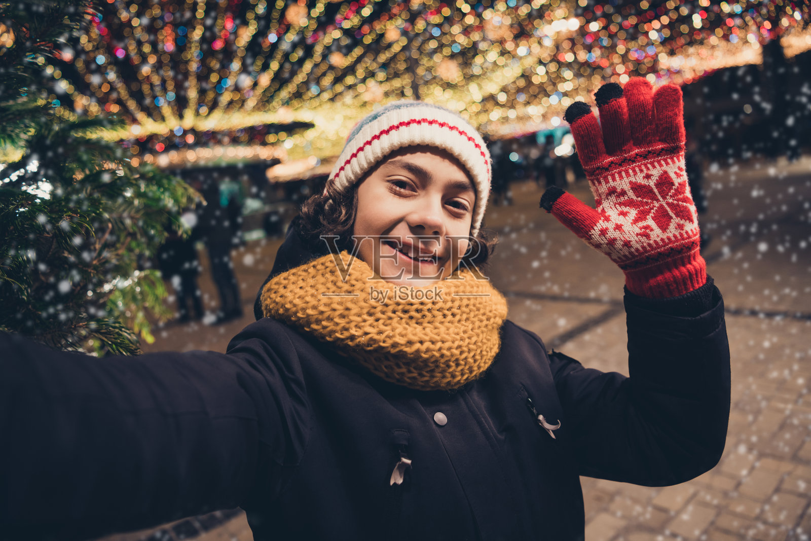 快乐可爱的男孩穿着外套，在城市集市的圣诞氛围中享受，录制视频并挥手。照片摄影图片