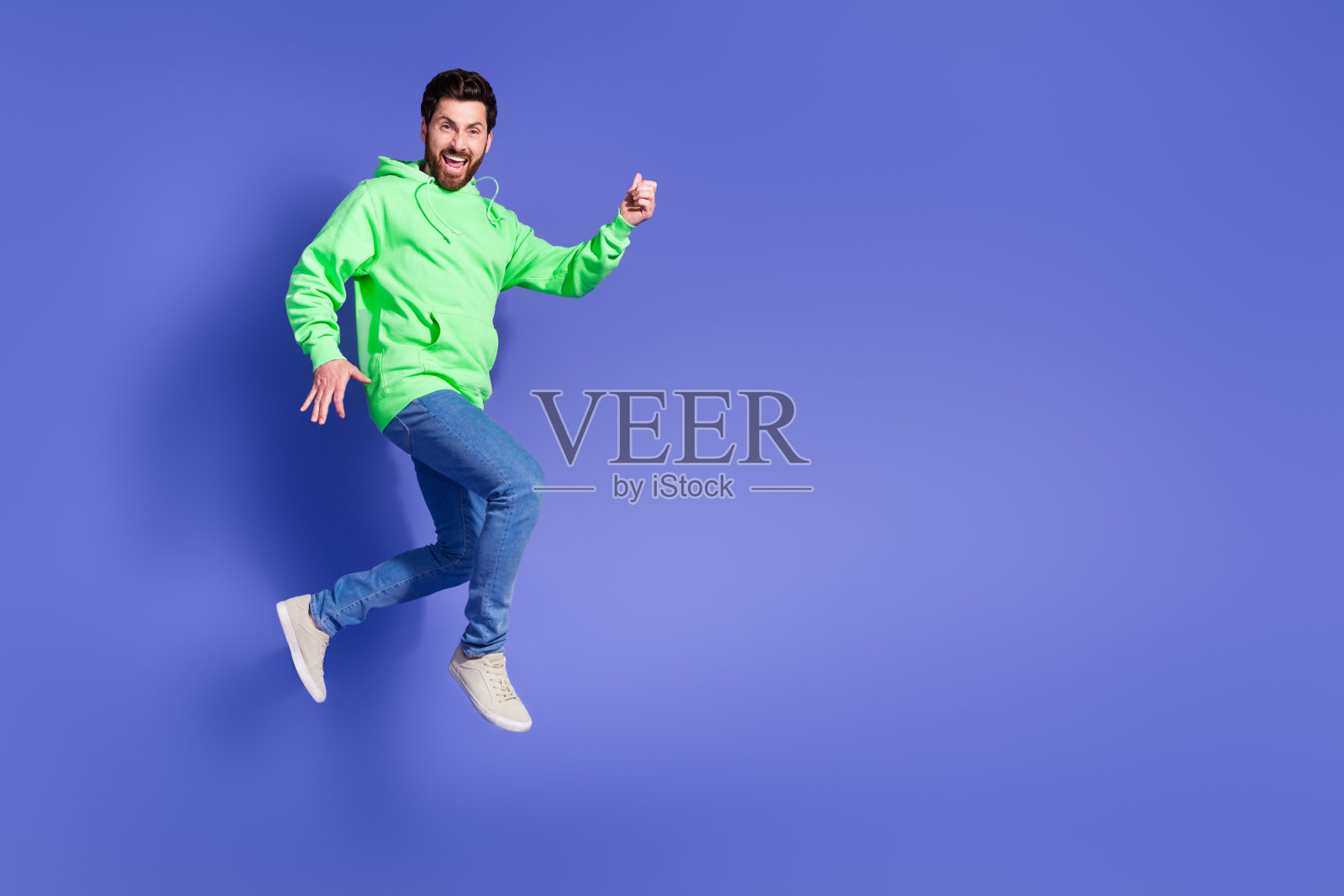 全身照：穿着时尚绿色服装的年轻帅气男性在紫色背景上匆忙奔跑照片摄影图片