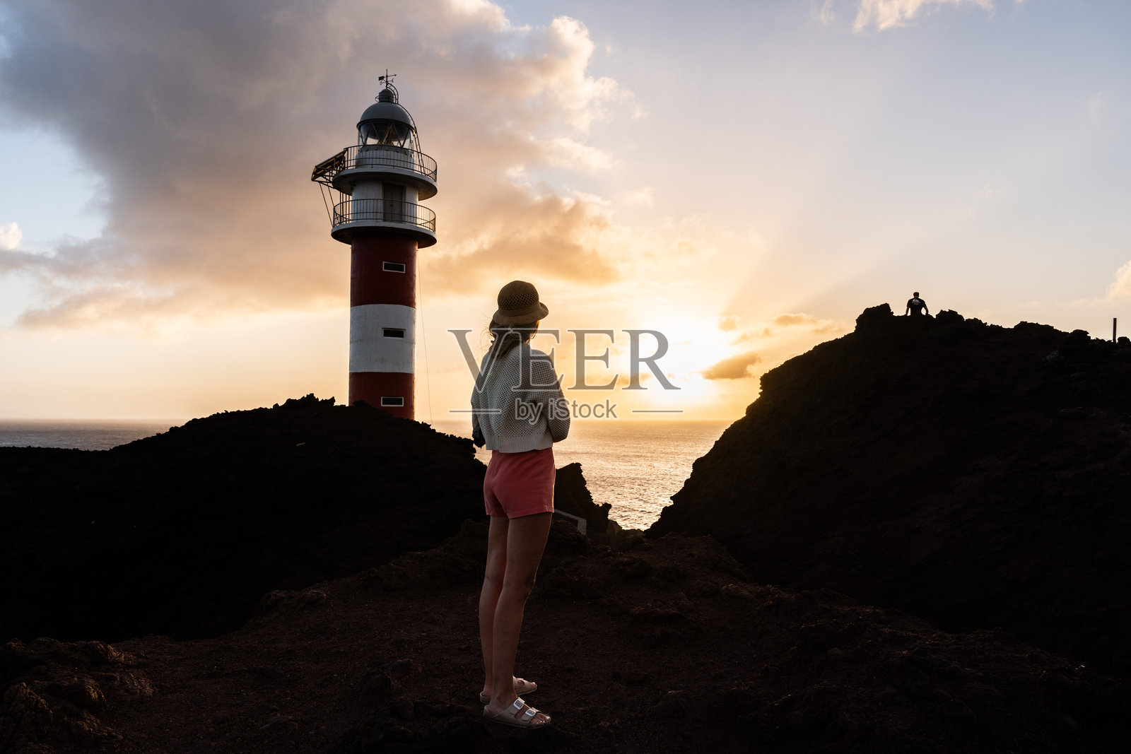 一位女性在灯塔旁欣赏海洋上的日落。照片摄影图片