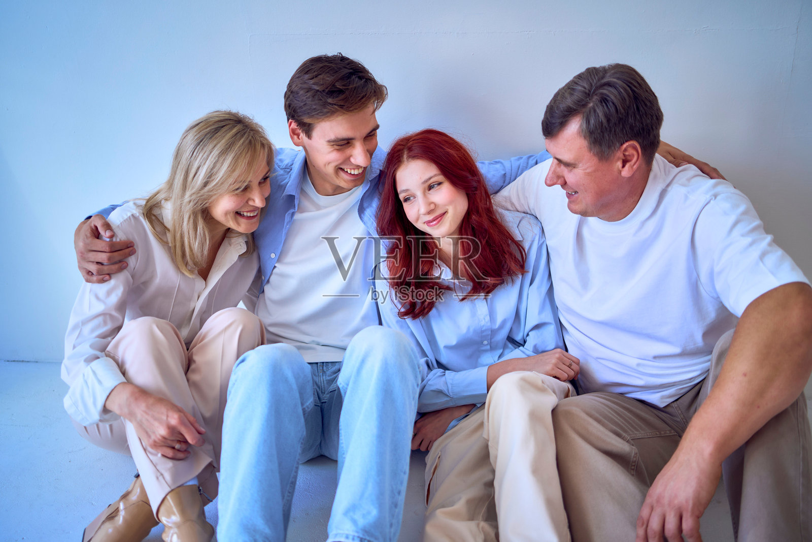 一家人，中年夫妻，年轻的儿子和青少女女儿，坐在白色背景前，摄影棚拍摄。照片摄影图片