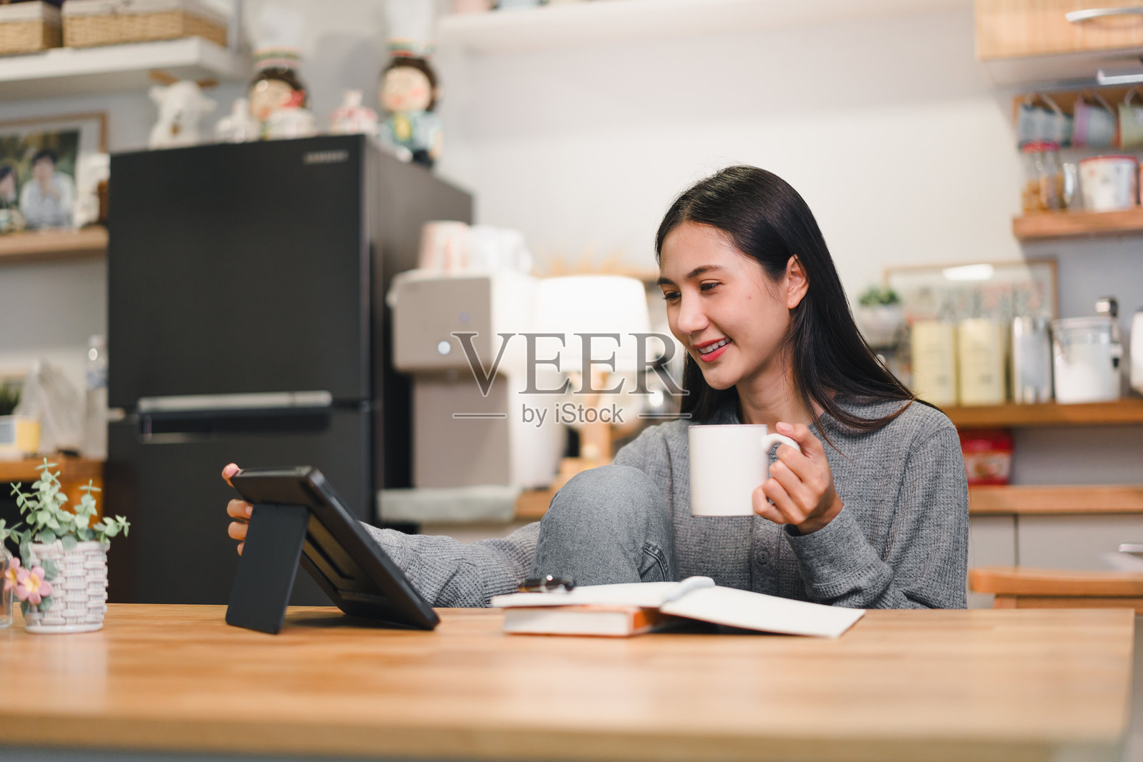 女人在家中享受温馨时刻，边喝咖啡边使用平板。温暖的氛围和放松的环境营造出舒适和满足感。照片摄影图片