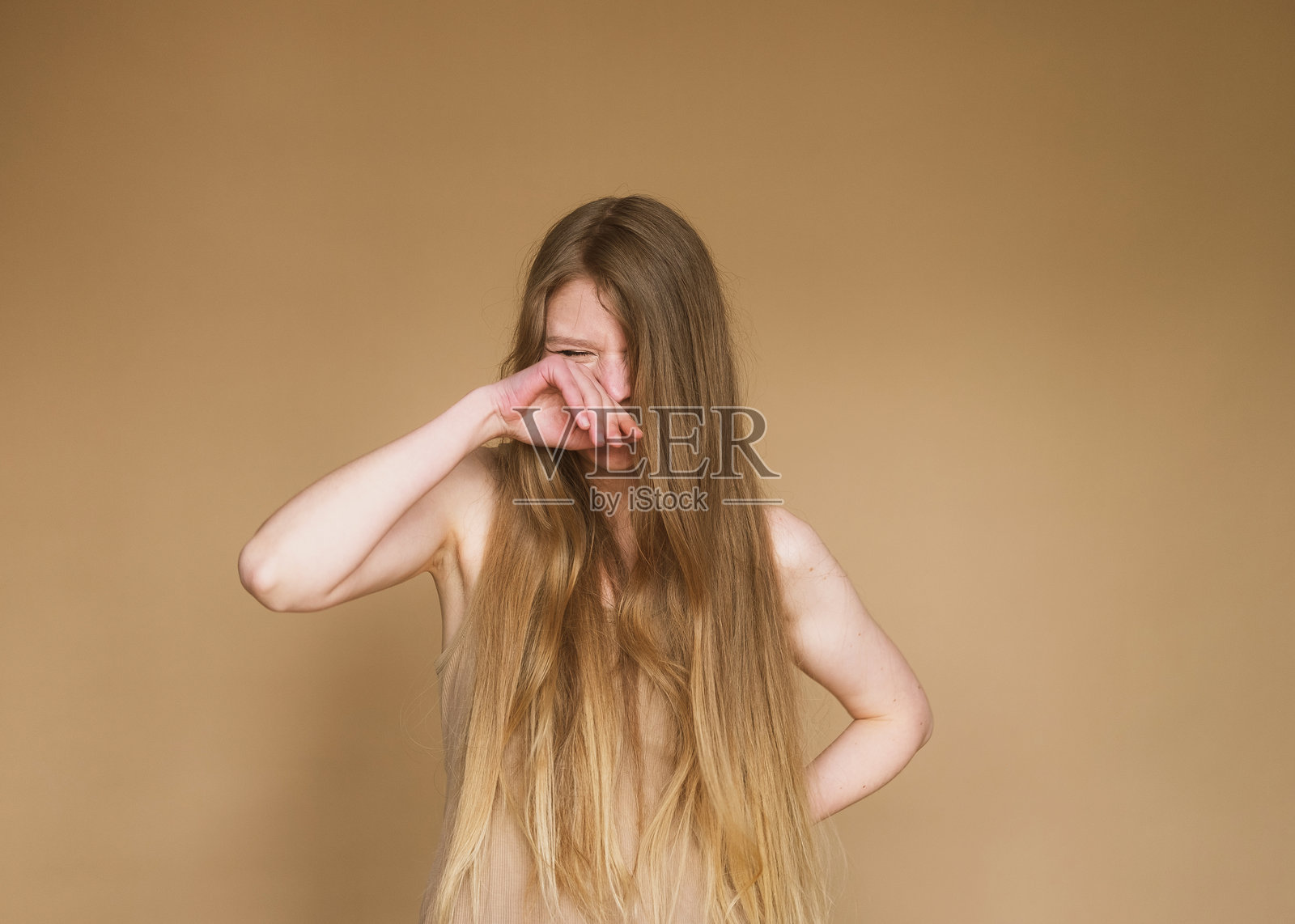 年轻女子长发披肩，哭泣时用手遮住脸。照片摄影图片