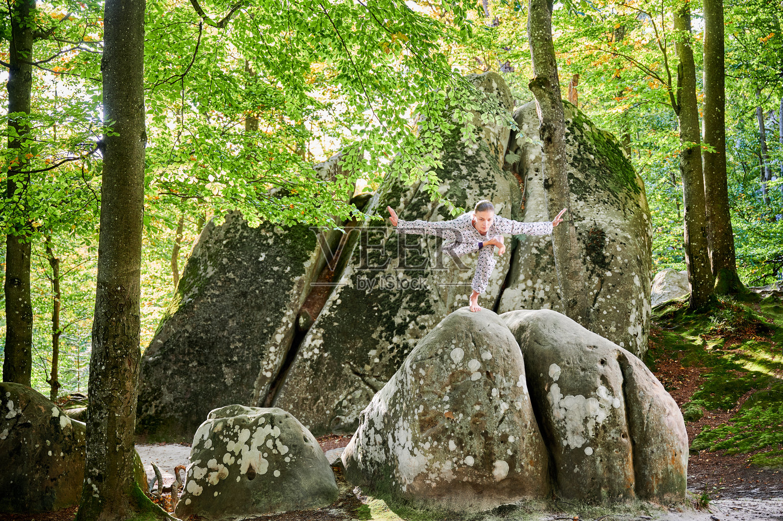 女性在森林中户外练习瑜伽。赤脚的女性站在瑜伽垫上，周围是树木和岩石。照片摄影图片