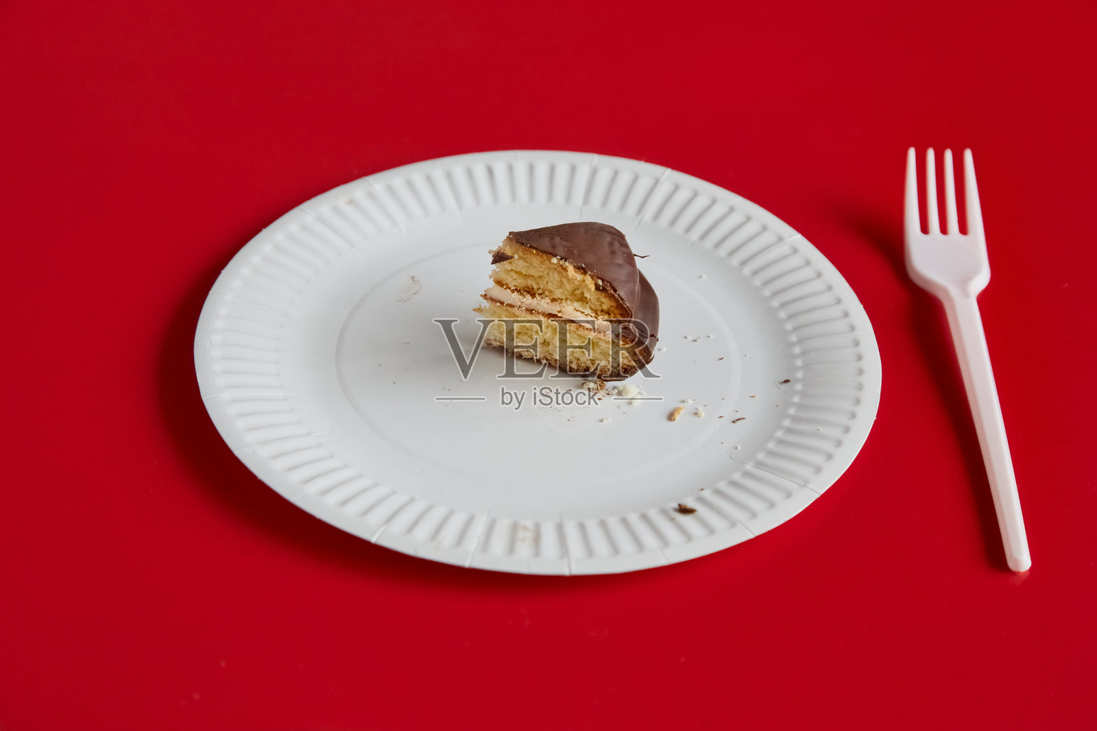一小块巧克力派放在白色一次性盘子上，背景是红色，旁边有一把白色一次性叉子，适合分享的派，适合减肥。照片摄影图片