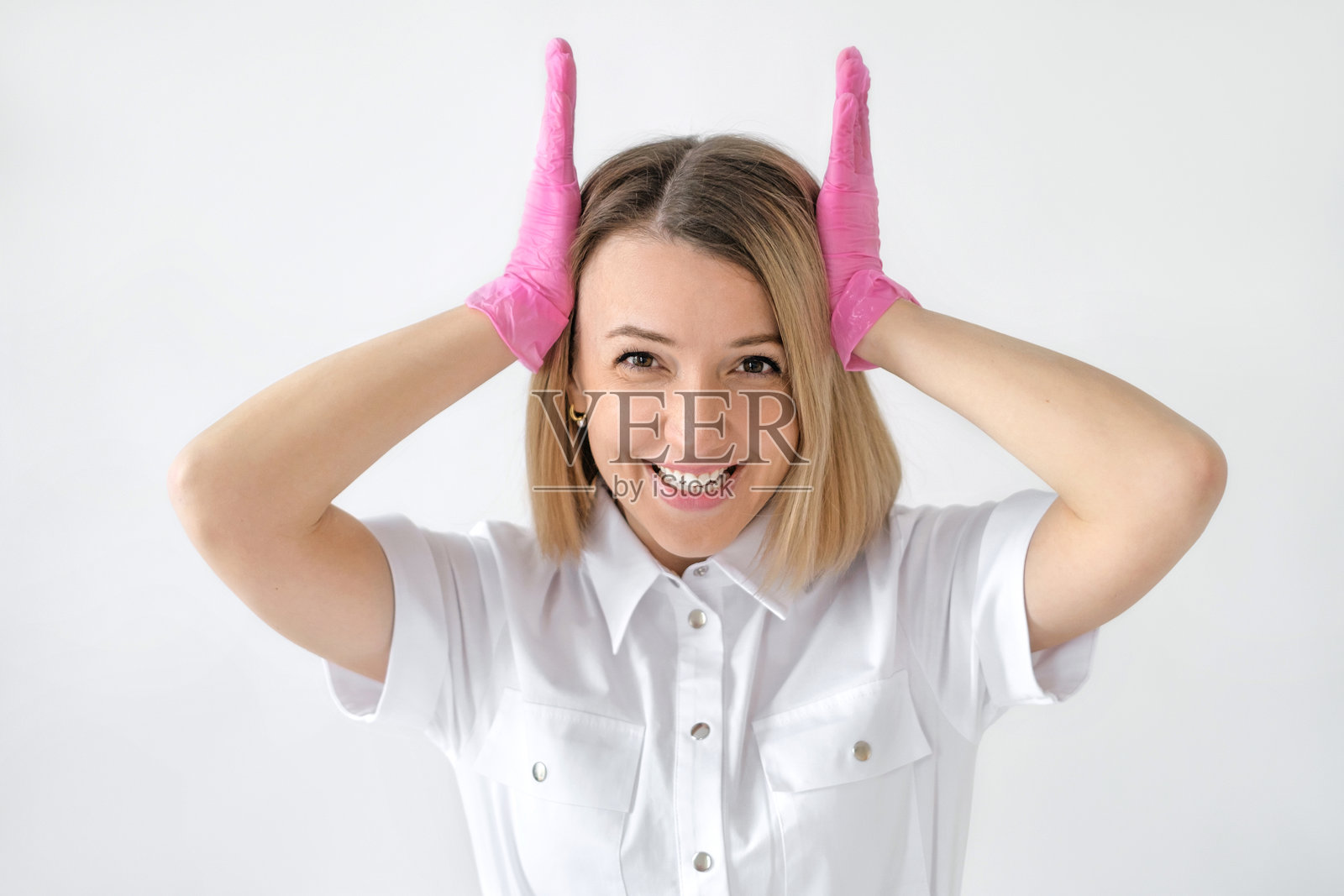 一位穿着医疗制服和粉色手套的女医生笑着，因脑部压力和信息过载而捂住头部。照片摄影图片