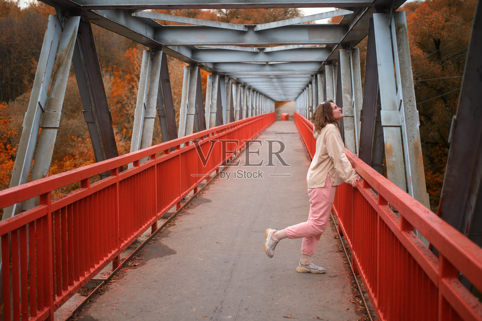 成年女性在混凝土桥上摆姿势，金属梁高耸于街道之上。照片摄影图片