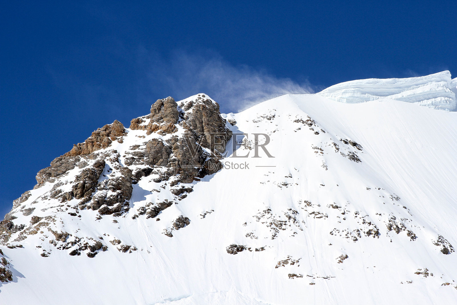 瑞士伯尔尼阿尔卑斯山峰上，雪花在湛蓝的天空中飞舞照片摄影图片
