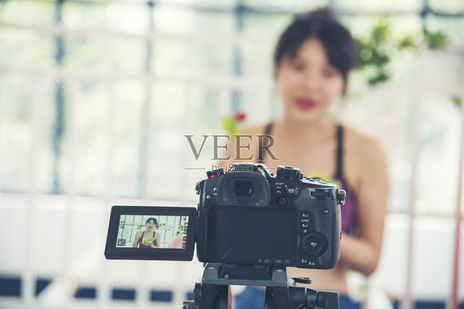 亚洲网红博主在家厨房进行健康生活方式的直播评测。年轻女性博主快乐地分享素食产品，享用蔬菜和水果。健康微笑的女性社交媒体博主直播。照片摄影图片