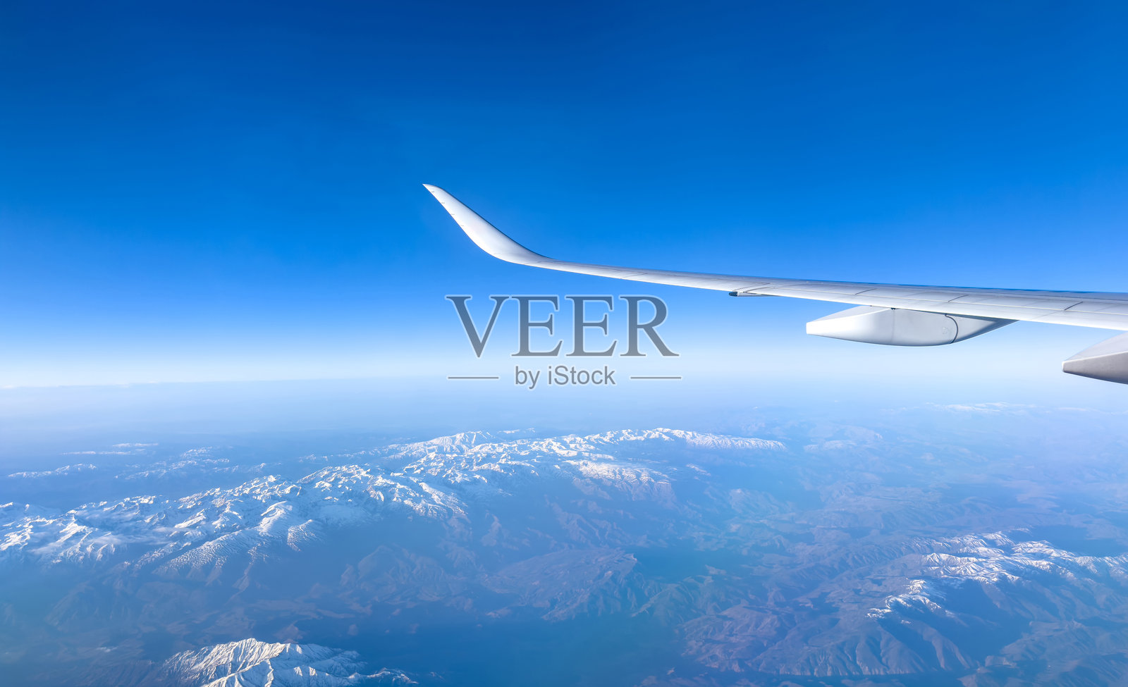 飞机飞越雪山，透过飞机窗户的视角，蓝天。照片摄影图片