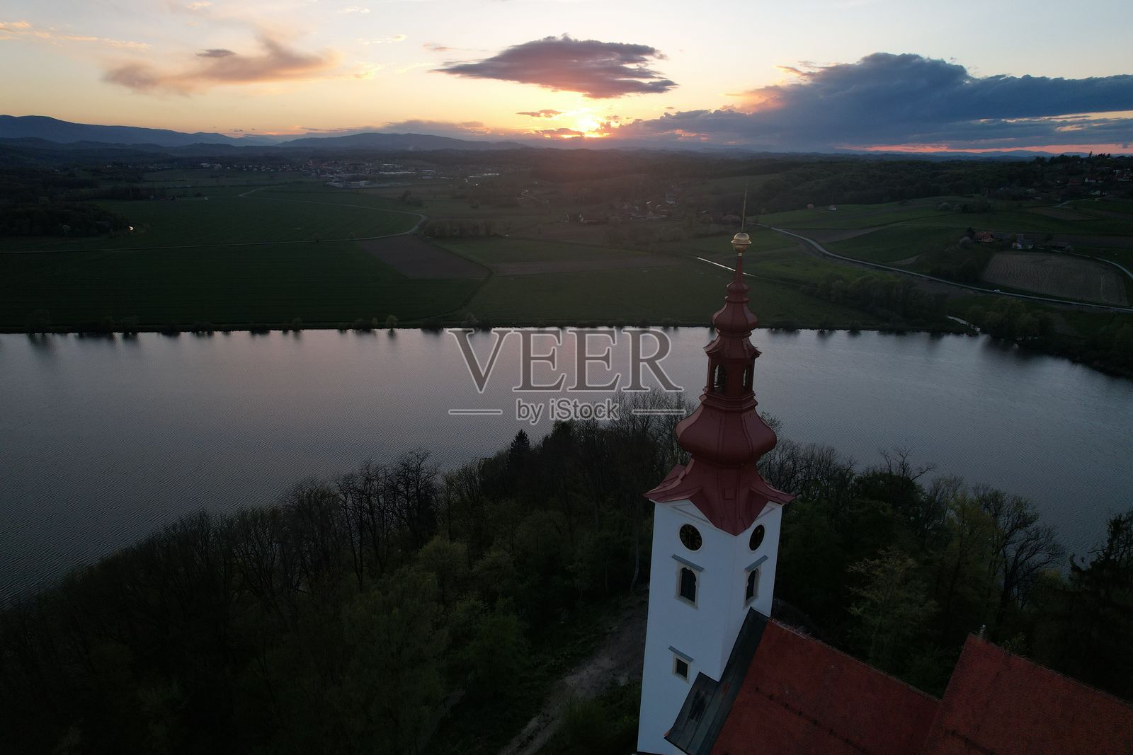 河流风景上的日落与教堂塔楼。照片摄影图片