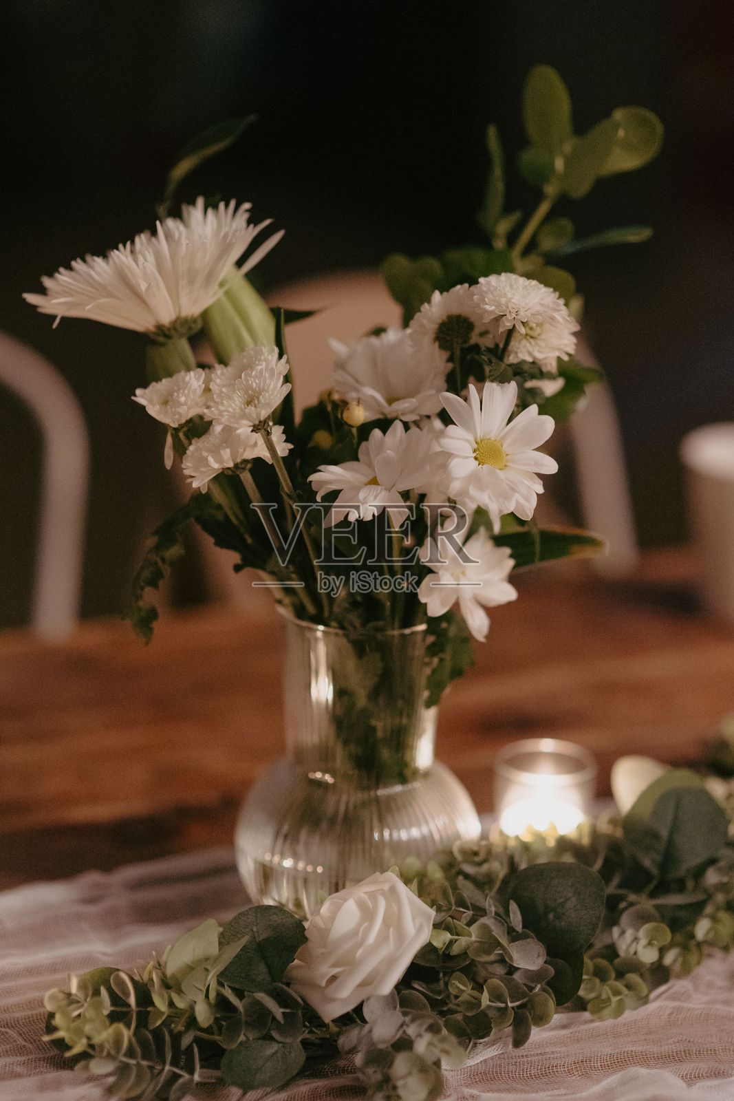 一个装满白色雏菊和康乃馨的花瓶放在木桌上。照片摄影图片