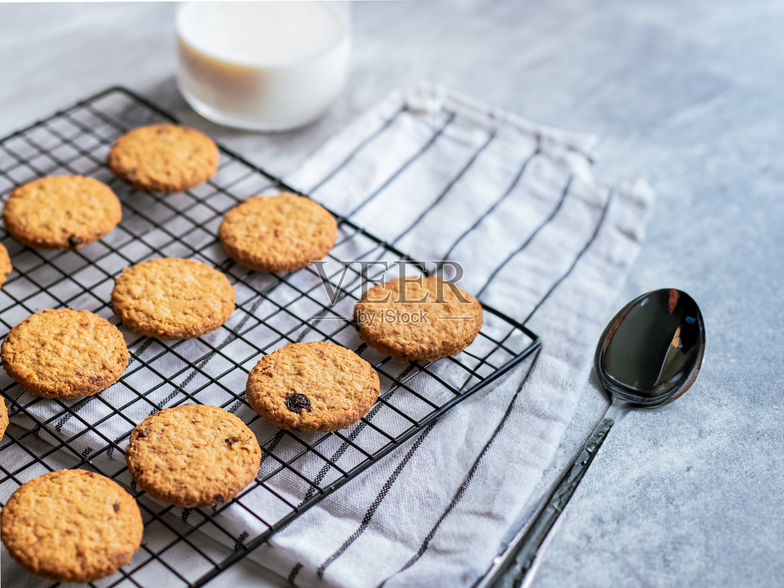 新鲜出炉的燕麦饼干在黑色铁架上冷却，背景明亮，柔和的自然光照射。饼干呈金棕色，带有葡萄干的点缀，外脆内软，营造出温馨的氛围。照片摄影图片