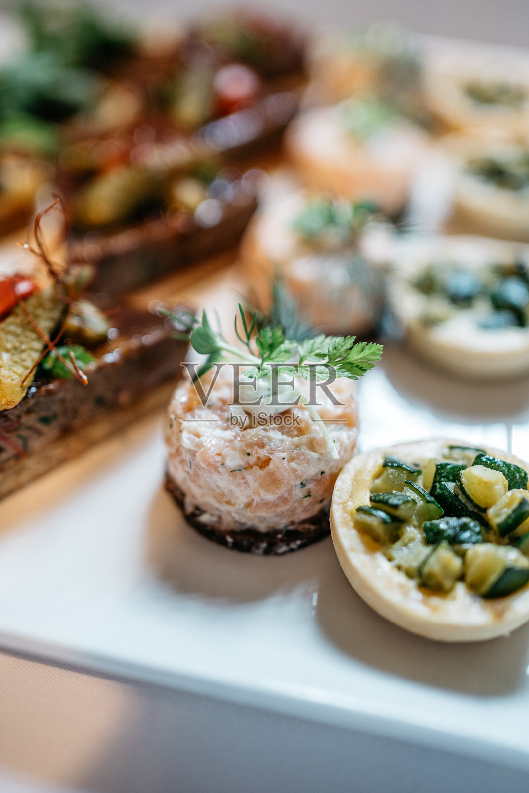 精致的开胃菜，白盘上摆放着三文鱼塔塔和开放式三明治照片摄影图片