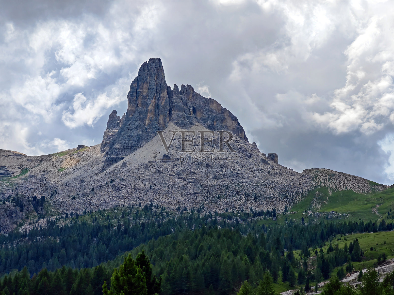 雄伟的梅佐迪山峰高耸于多洛米蒂山脉的郁郁葱葱的森林之上，笼罩在多云的天空下。照片摄影图片