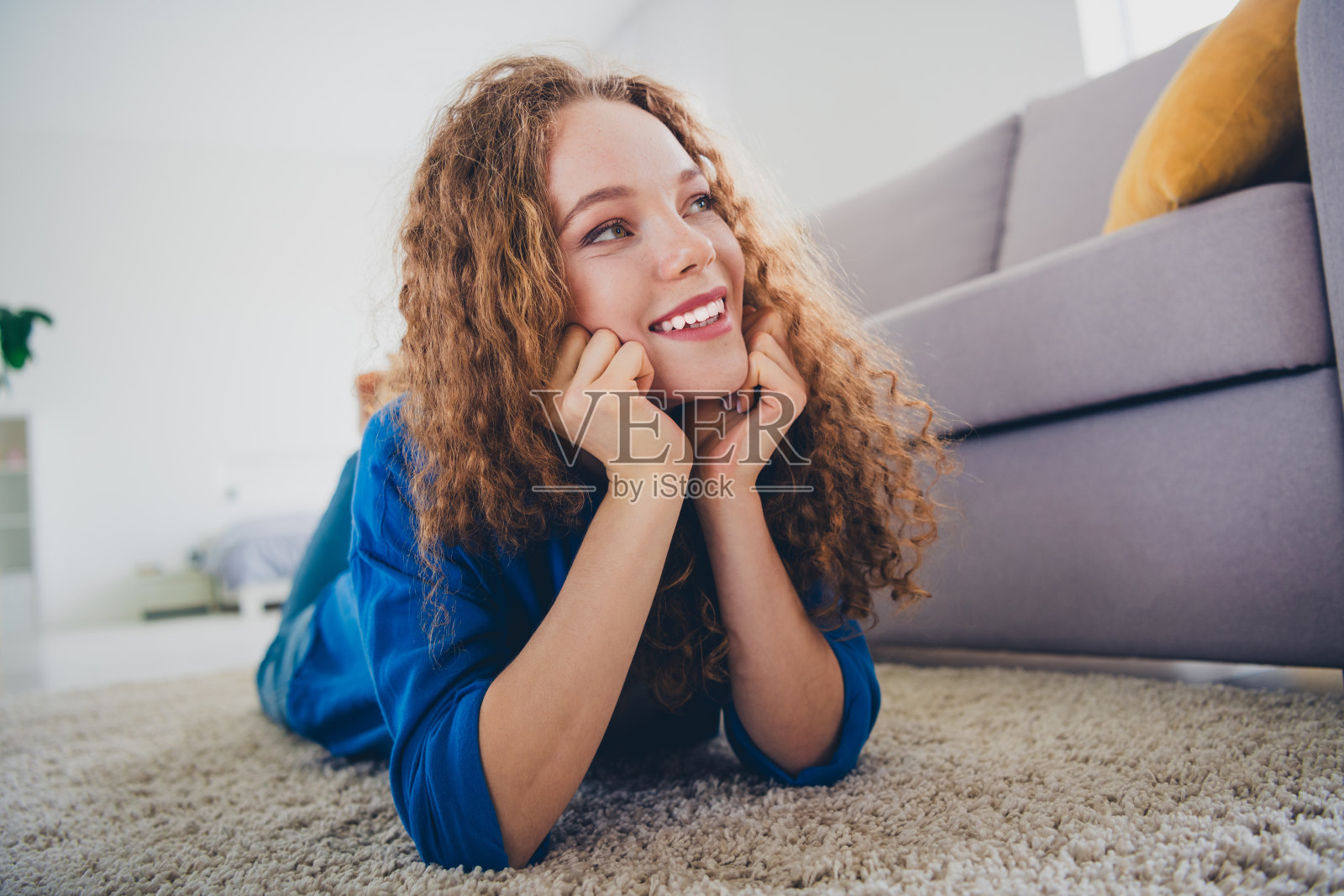 可爱的梦幻女孩穿着蓝色衬衫，躺在地板上休息，享受周末的室内时光。照片摄影图片