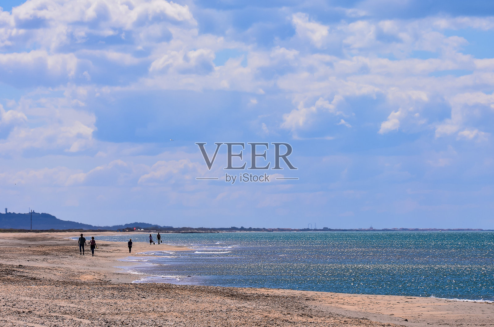 沙滩上有人在沙子上行走，背景是一片水域照片摄影图片