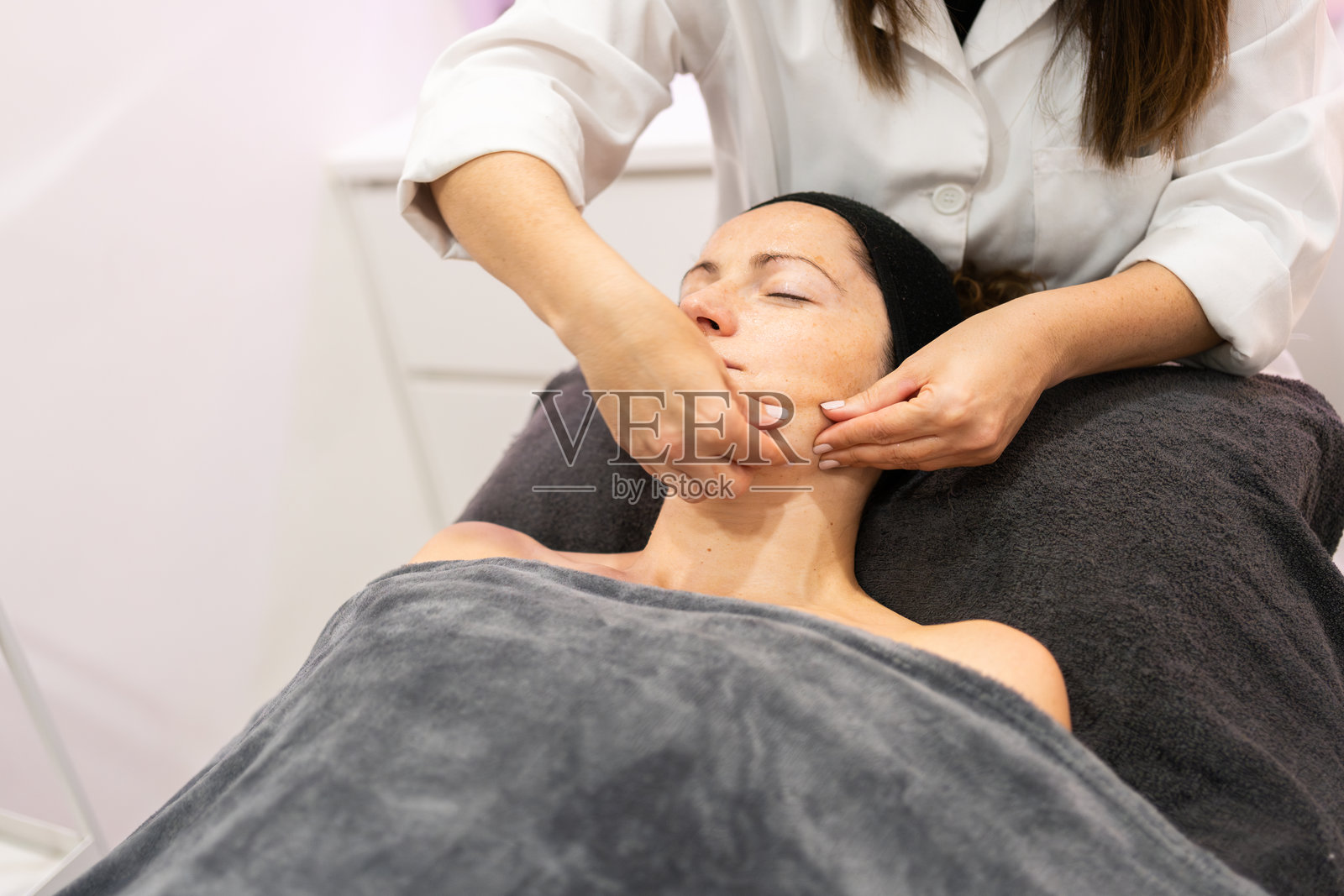 美容院中，美容师为客户面部按摩的美容疗程剪影照片摄影图片