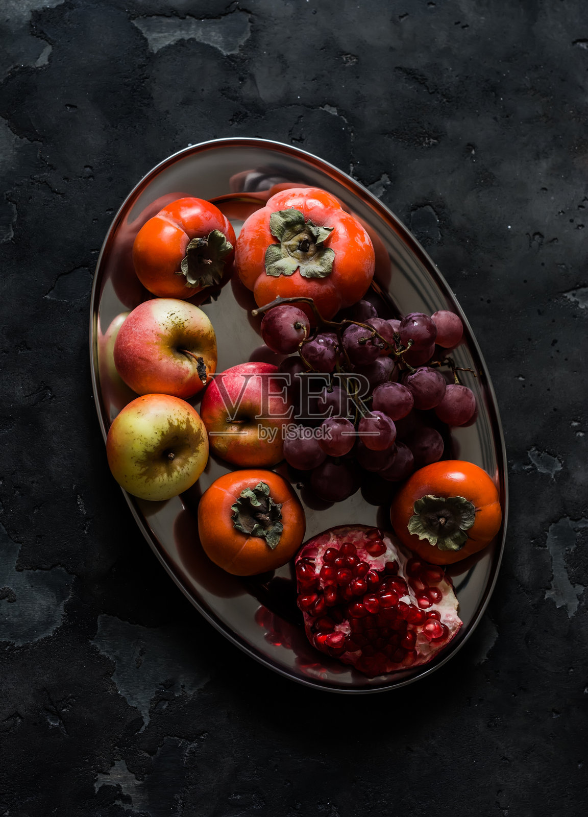 季节性水果 - 柿子、红葡萄、苹果、石榴在深色背景上，俯视图照片摄影图片