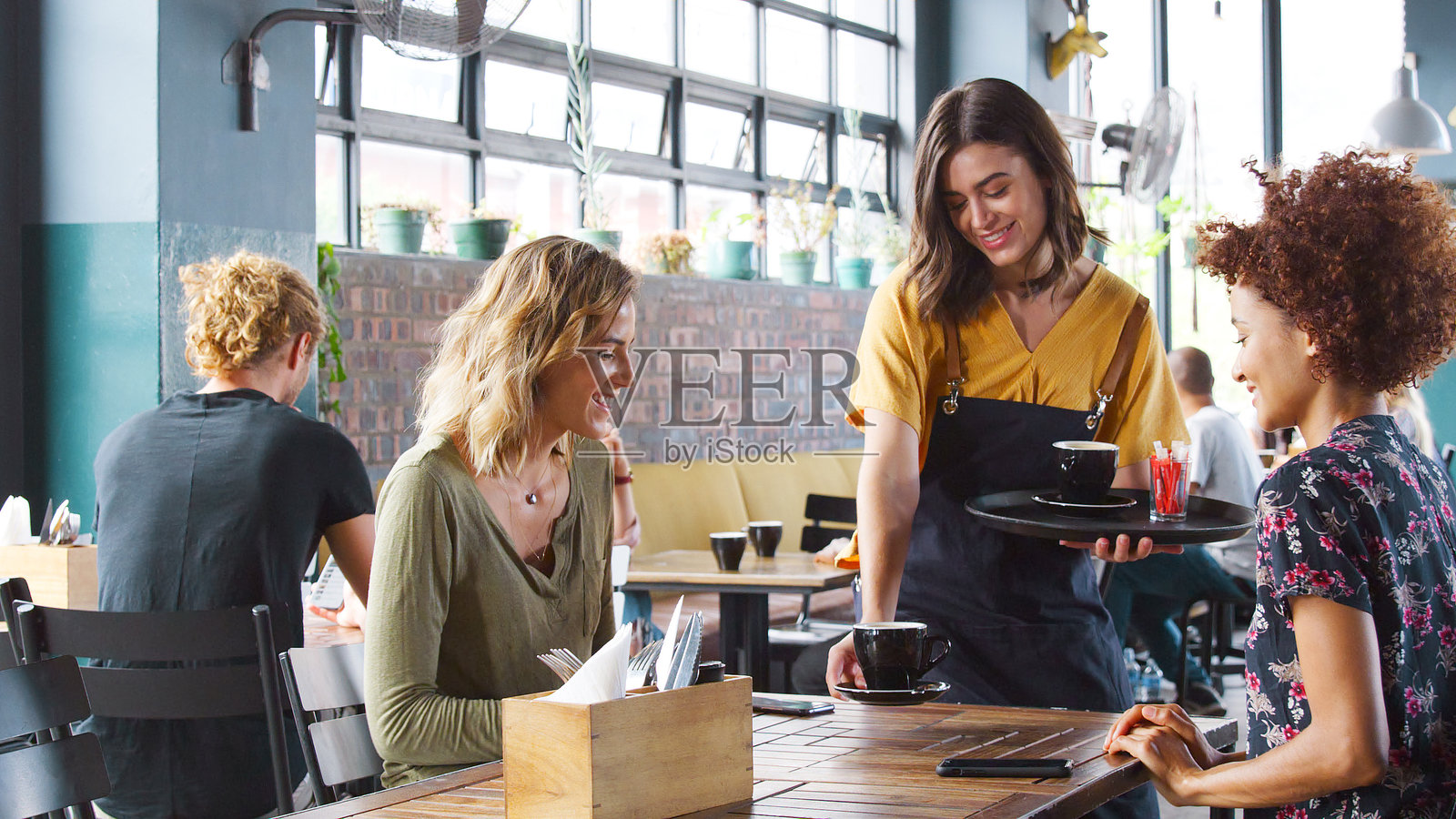 两个年轻朋友坐在咖啡店的桌子旁，女服务员正在给他们送饮料。照片摄影图片