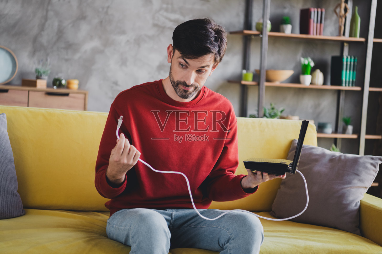 中年男子穿着休闲毛衣，思考路由器连接，享受轻松的周末时光。照片摄影图片