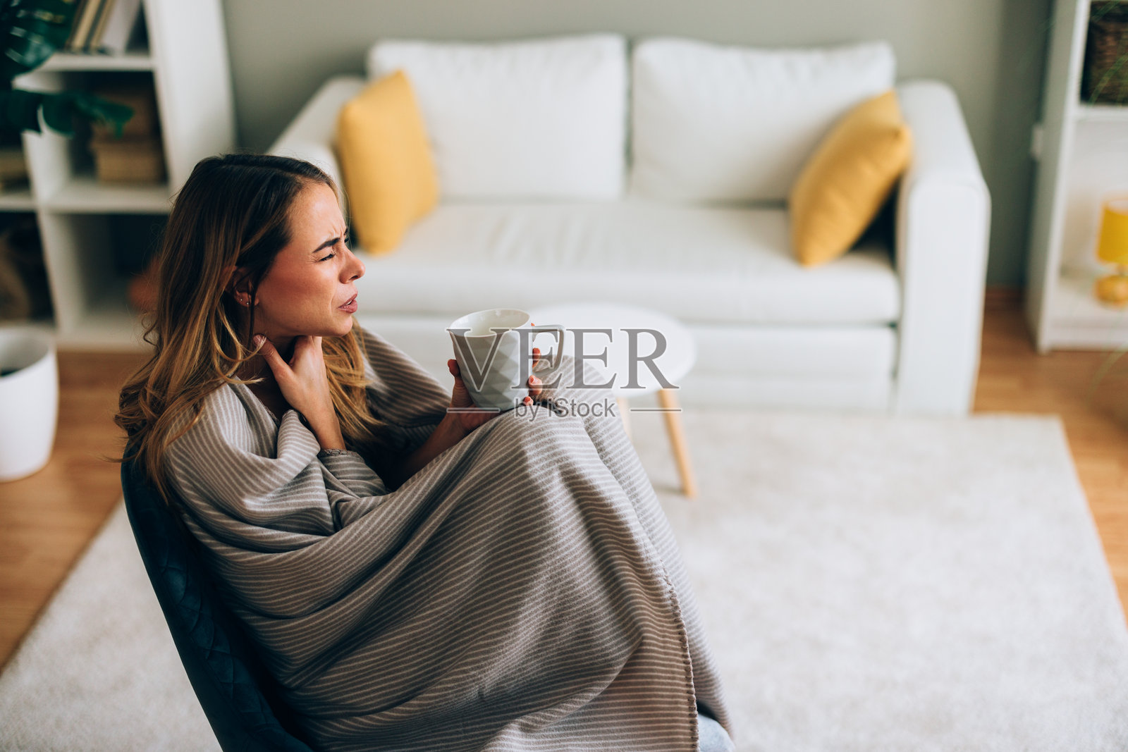 生病的女人在家中裹着毯子，手里拿着温暖的饮品照片摄影图片