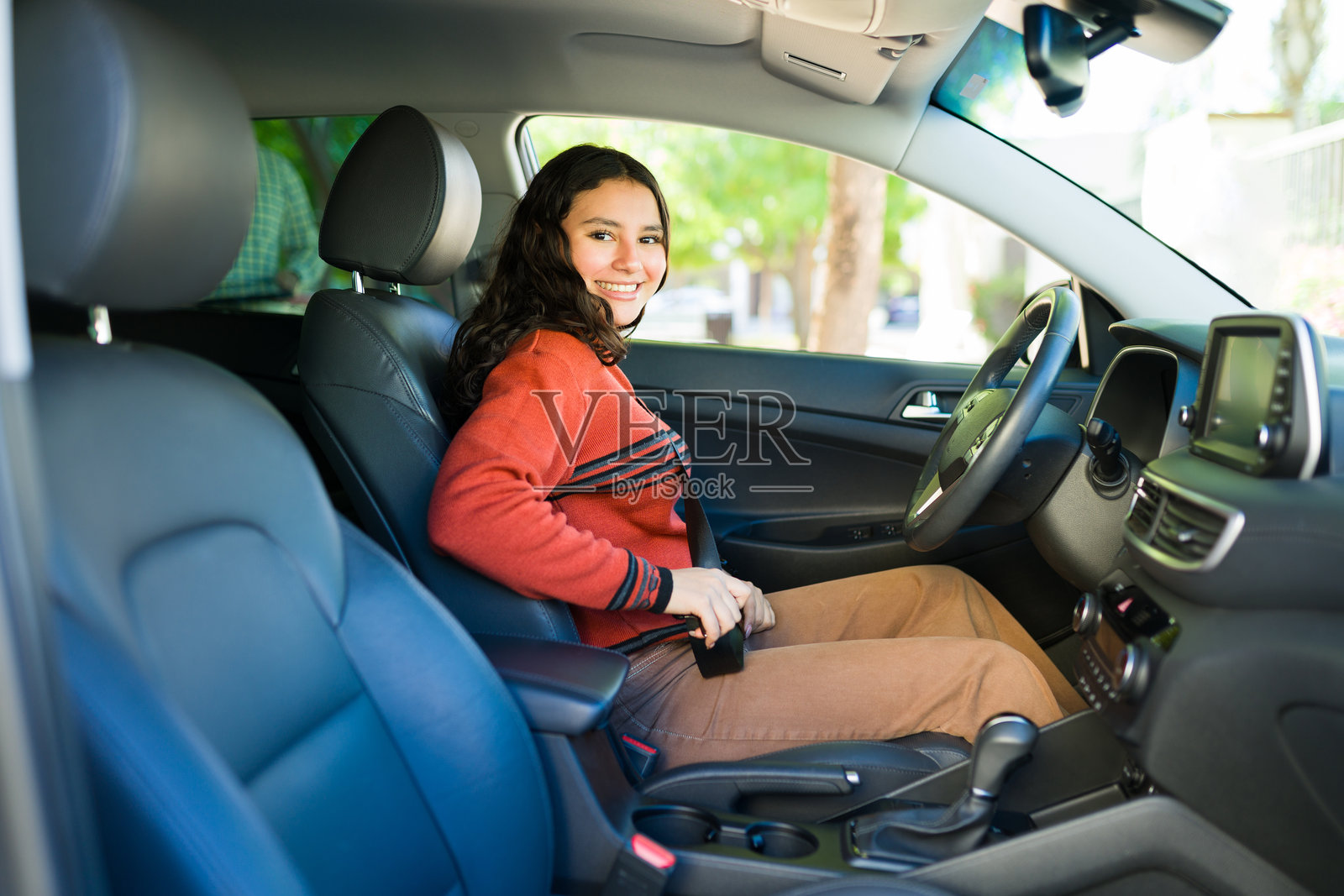 坐在驾驶座上的少女微笑着系好安全带，为即将开始的安全旅程做好准备照片摄影图片