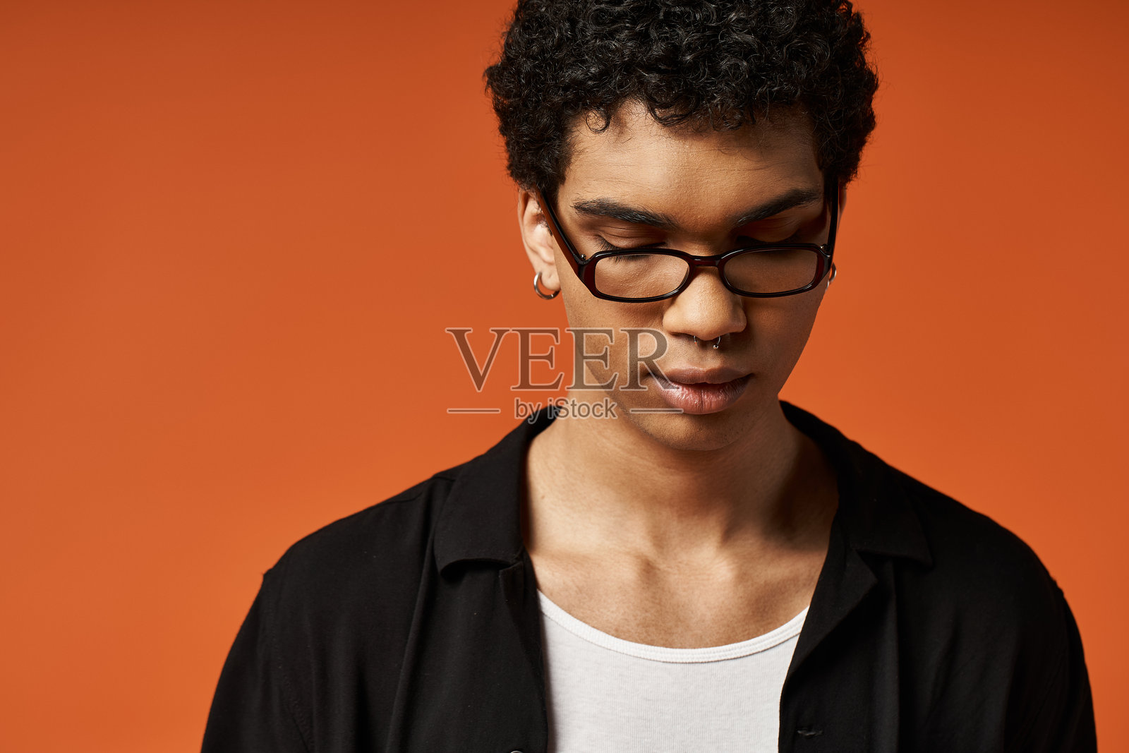 时尚的卷发男士戴着眼镜，悠闲地站在鲜艳的橙色背景前。照片摄影图片