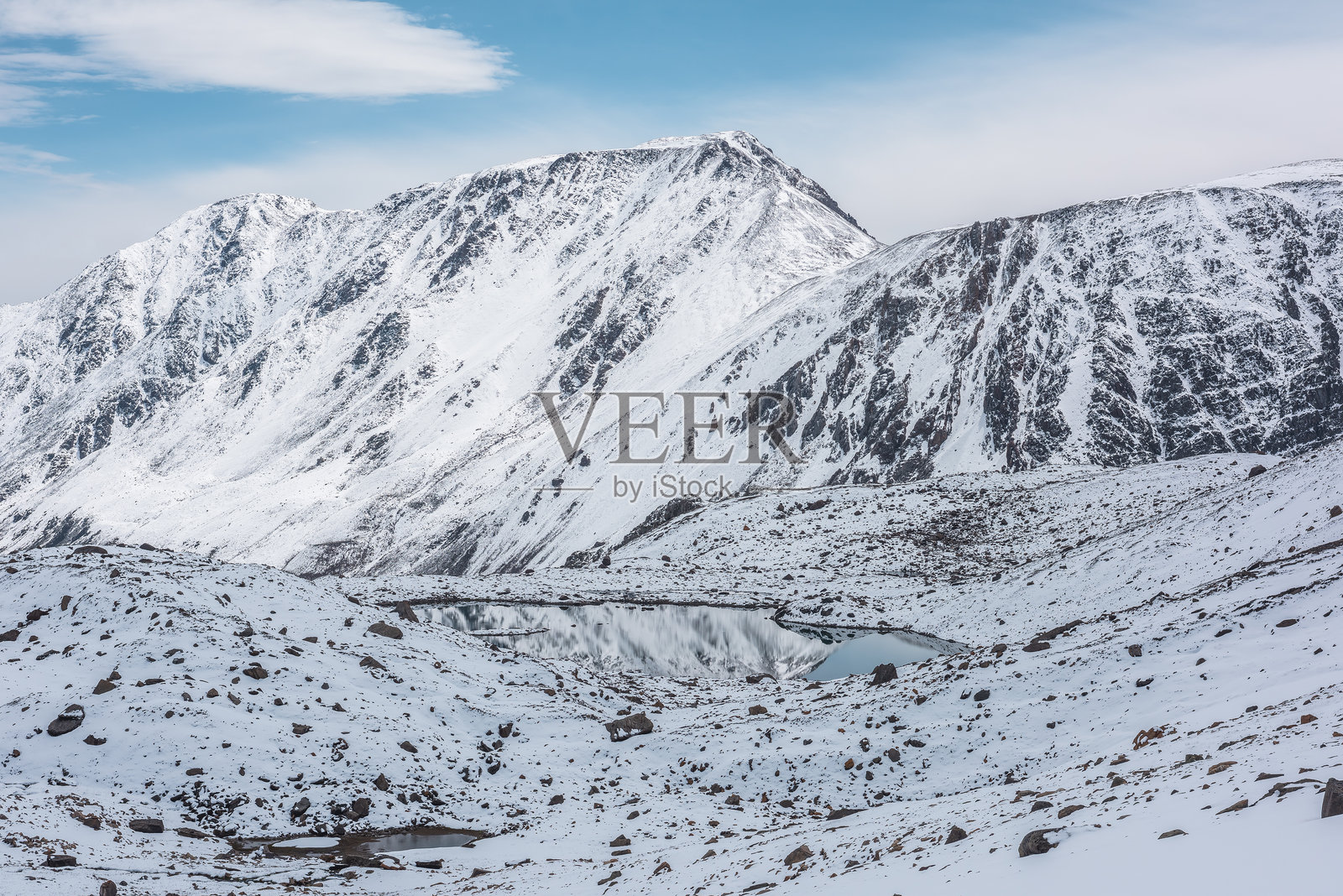 寒冷的雪白山谷景观，阿尔卑斯湖泊与被云层笼罩的雪山背景相映成趣。冰川湖泊、纯白的雪和高山中的石头在阳光明媚的日子里熠熠生辉。照片摄影图片