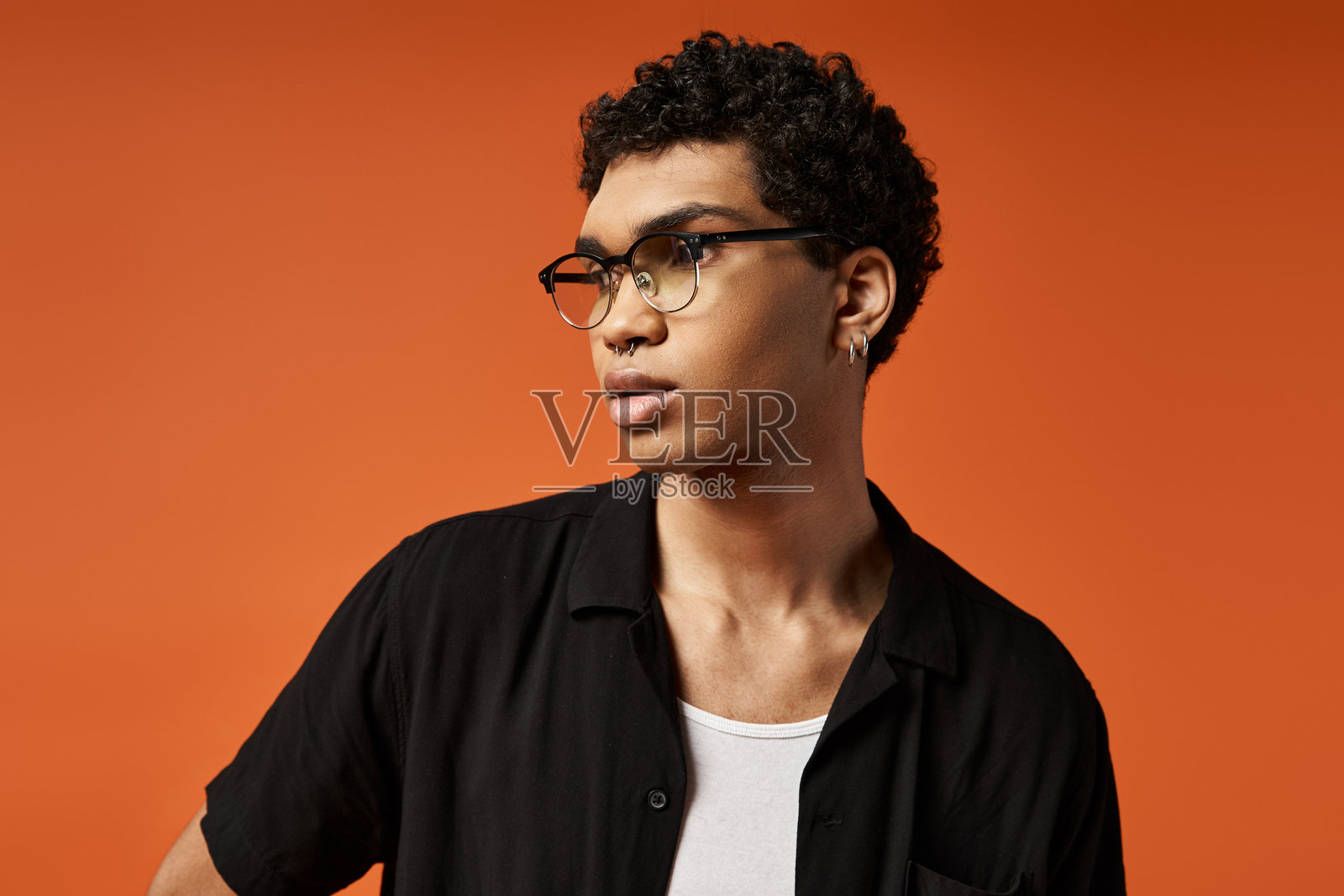 一位时尚的年轻男子自信地站在充满活力的橙色背景前，展示现代时尚。照片摄影图片