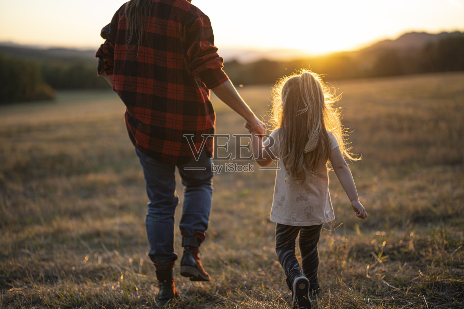 自然徒步旅行。母亲和孩子在日落时手牵手走路照片摄影图片