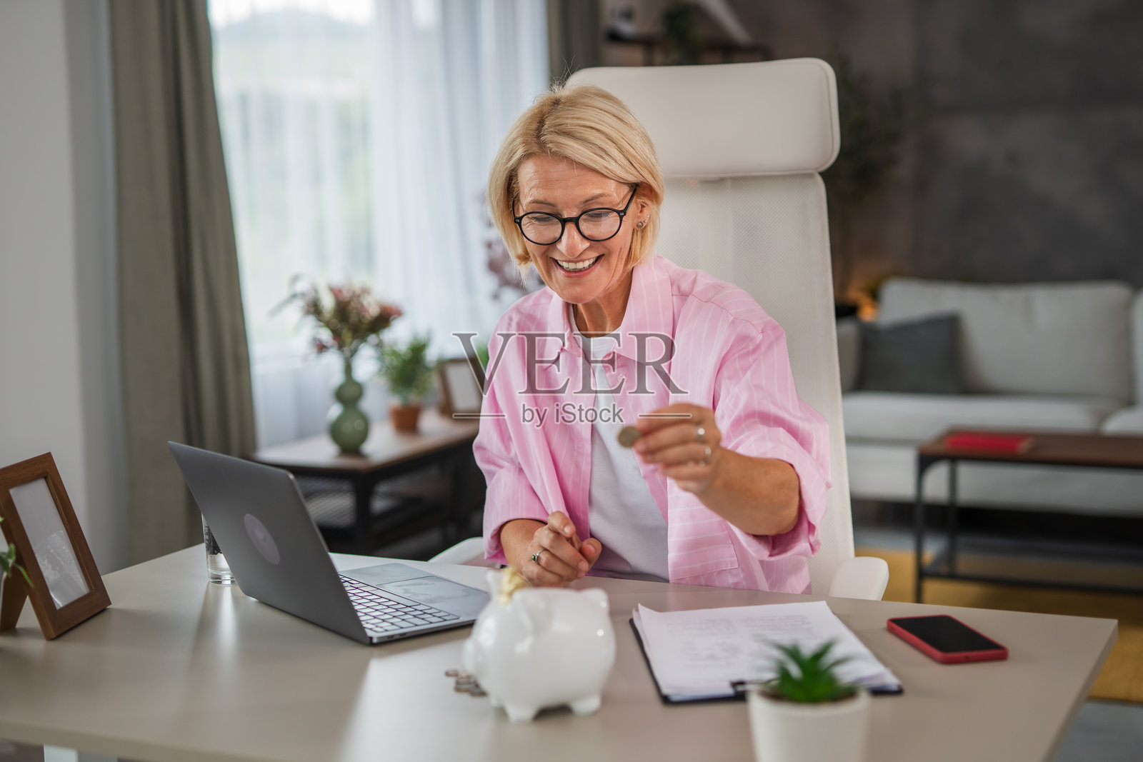 一位中年女性在家里支付账单并将钱存入储蓄罐，家庭财务概念照片摄影图片