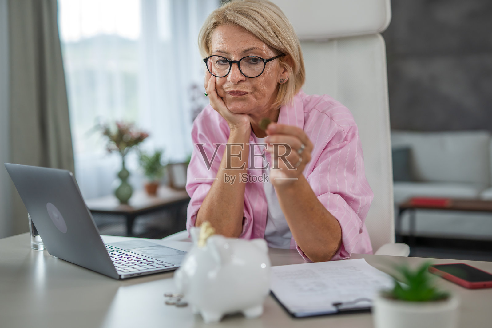 一位中年女性在家里支付账单并将钱存入储蓄罐，家庭财务概念照片摄影图片