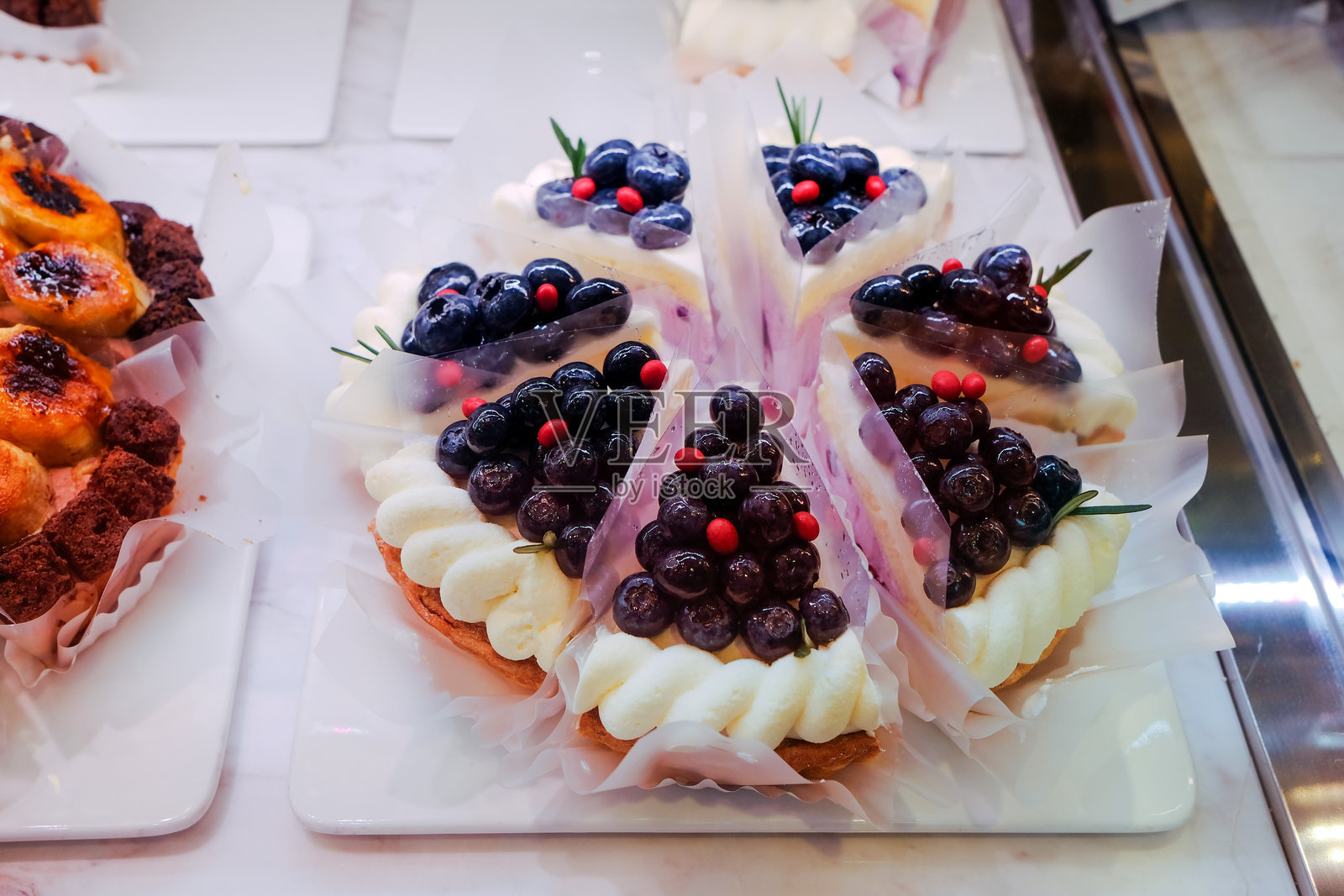 美味的奶油蛋糕切片特写，上面装饰着丰富的黑莓和覆盆子，放在玻璃展示柜中的大理石蛋糕托盘上，面包店的甜点。美丽的蛋糕待售。照片摄影图片