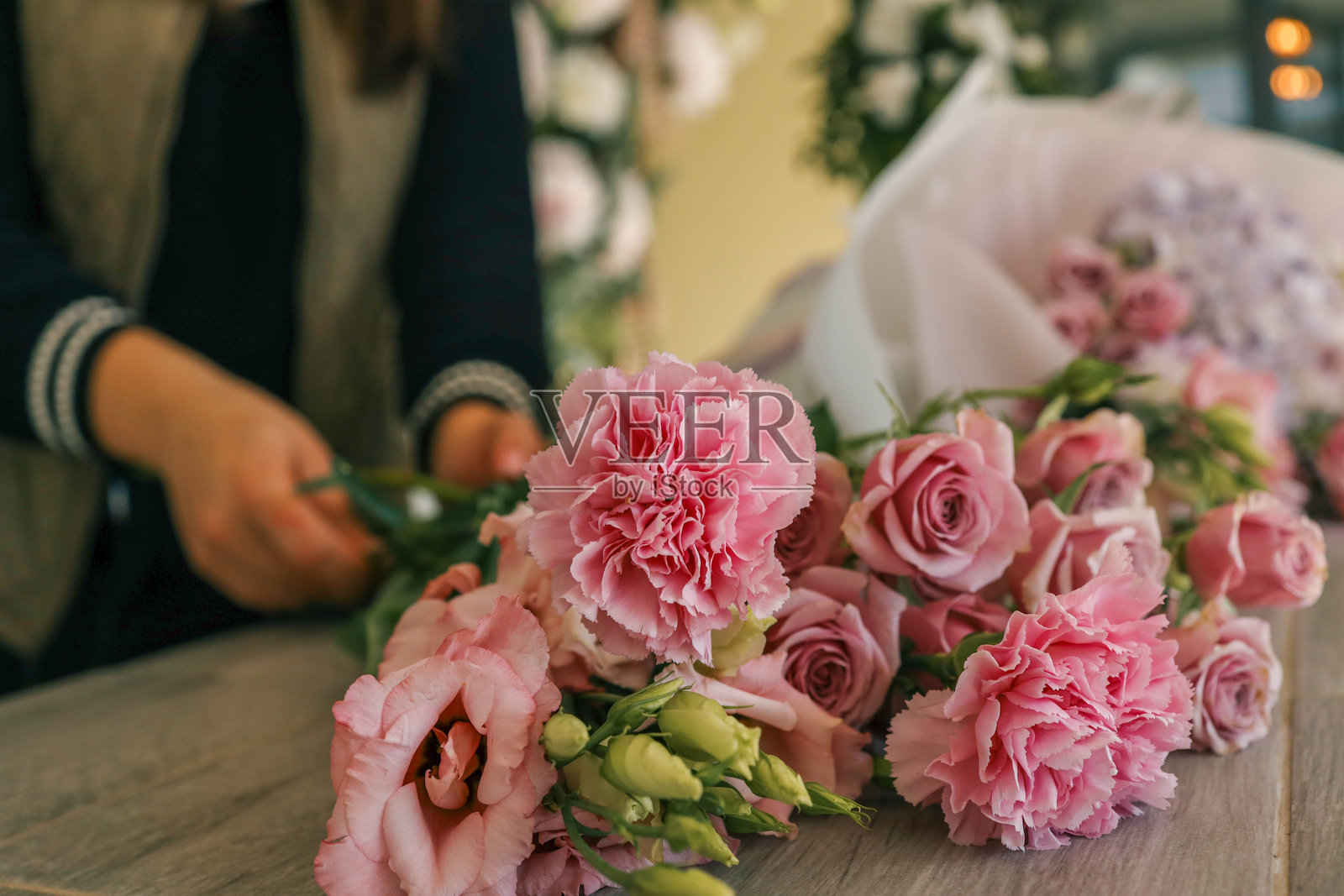 花店花艺师在木质柜台上整理粉色和柔和色调的花束，背景是模糊的花店。捕捉了花艺布置和自然美的精髓。照片摄影图片