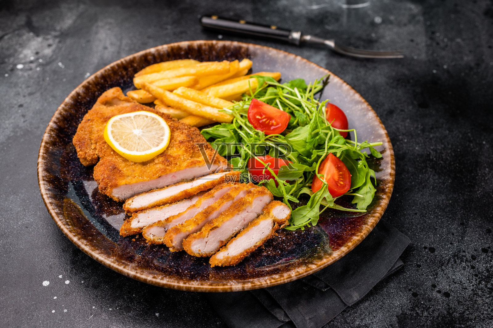 烤维也纳炸肉排，裹面包屑的肉配沙拉和薯条，放在盘子里。黑色背景。俯视图。照片摄影图片