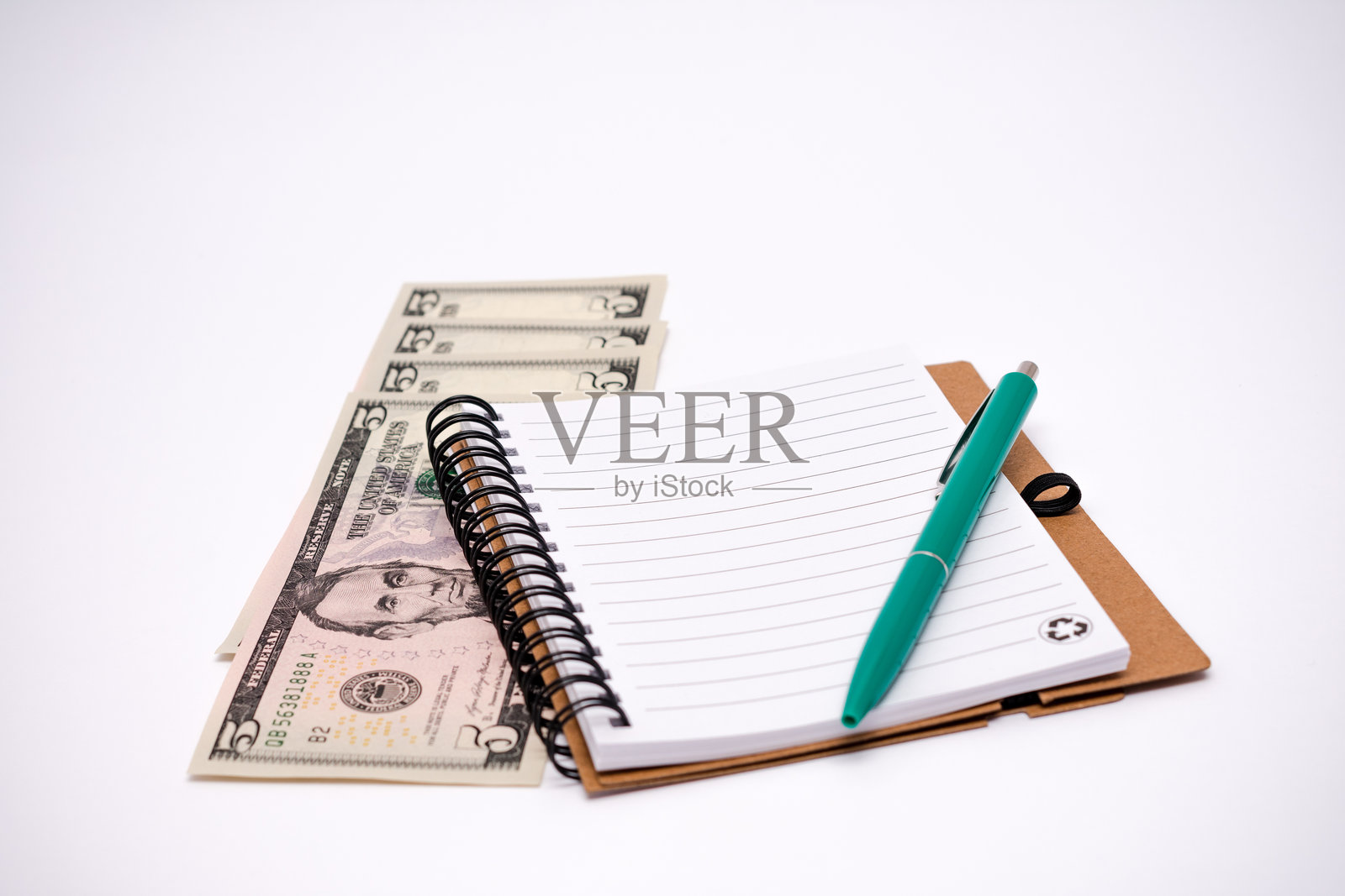 绿色钢笔放在一本有五美元钞票的笔记本上。照片摄影图片